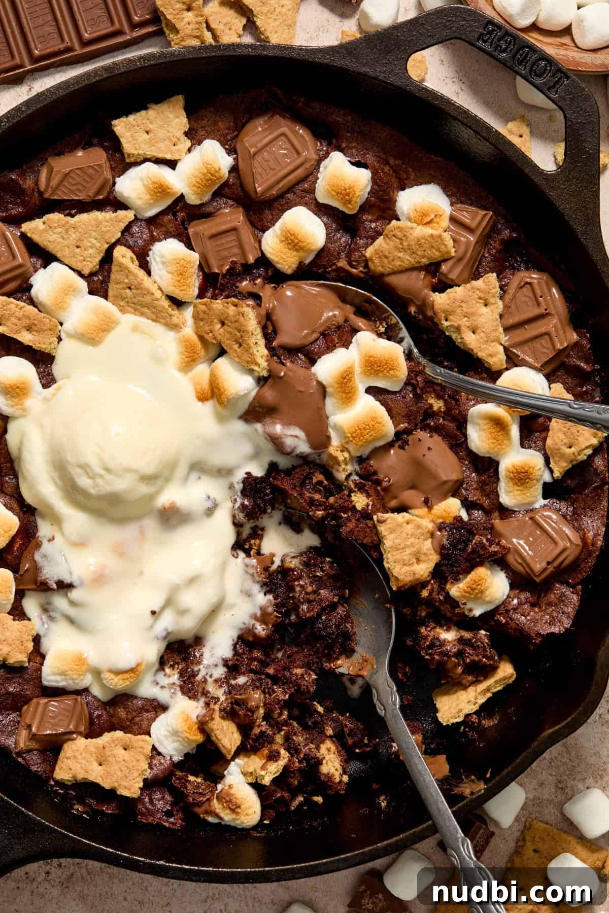 Skillet S'mores Brownie Recipe: Gooey Campfire Dessert 8 Overhead view of s'mores brownie in cast iron skillet with two spoons scooping into the brownie.