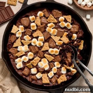 Skillet S'mores Brownie Recipe: Gooey Campfire Dessert 9 Brownie in skillet topped with marshmallows, chocolate bars and pieces of graham crackers.
