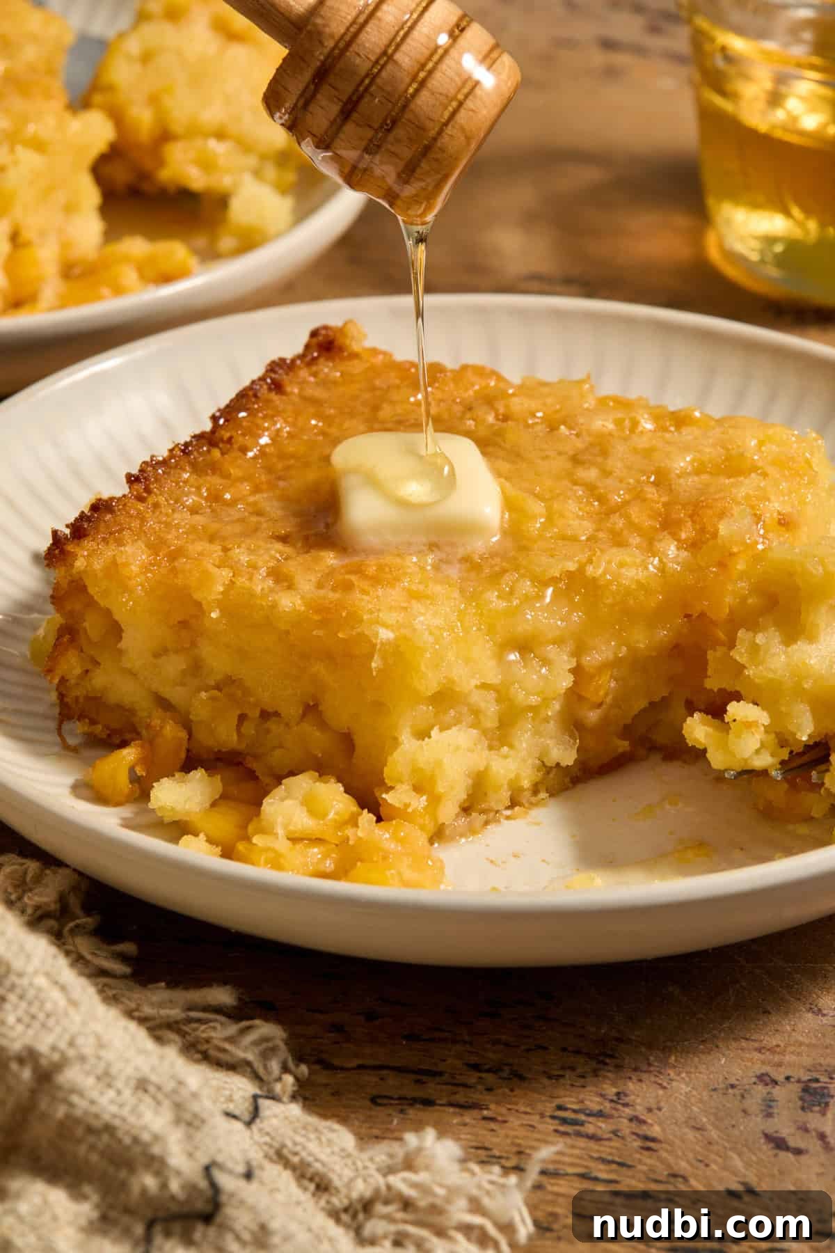 Sweet Honey Cornbread Casserole Recipe for Comforting Family Meals 2 Honey cornbread casserole served on plate with honey drizzling over butter on top.