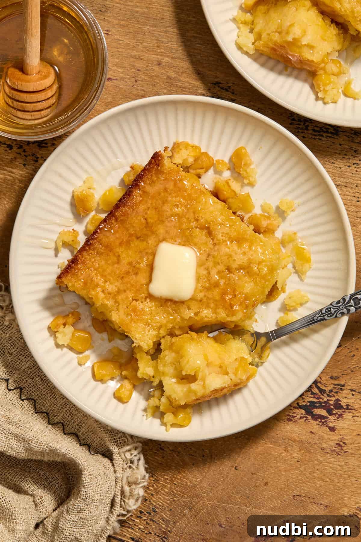 Sweet Honey Cornbread Casserole Recipe for Comforting Family Meals 12 Serving of cornbread casserole on plate with butter and honey on top.