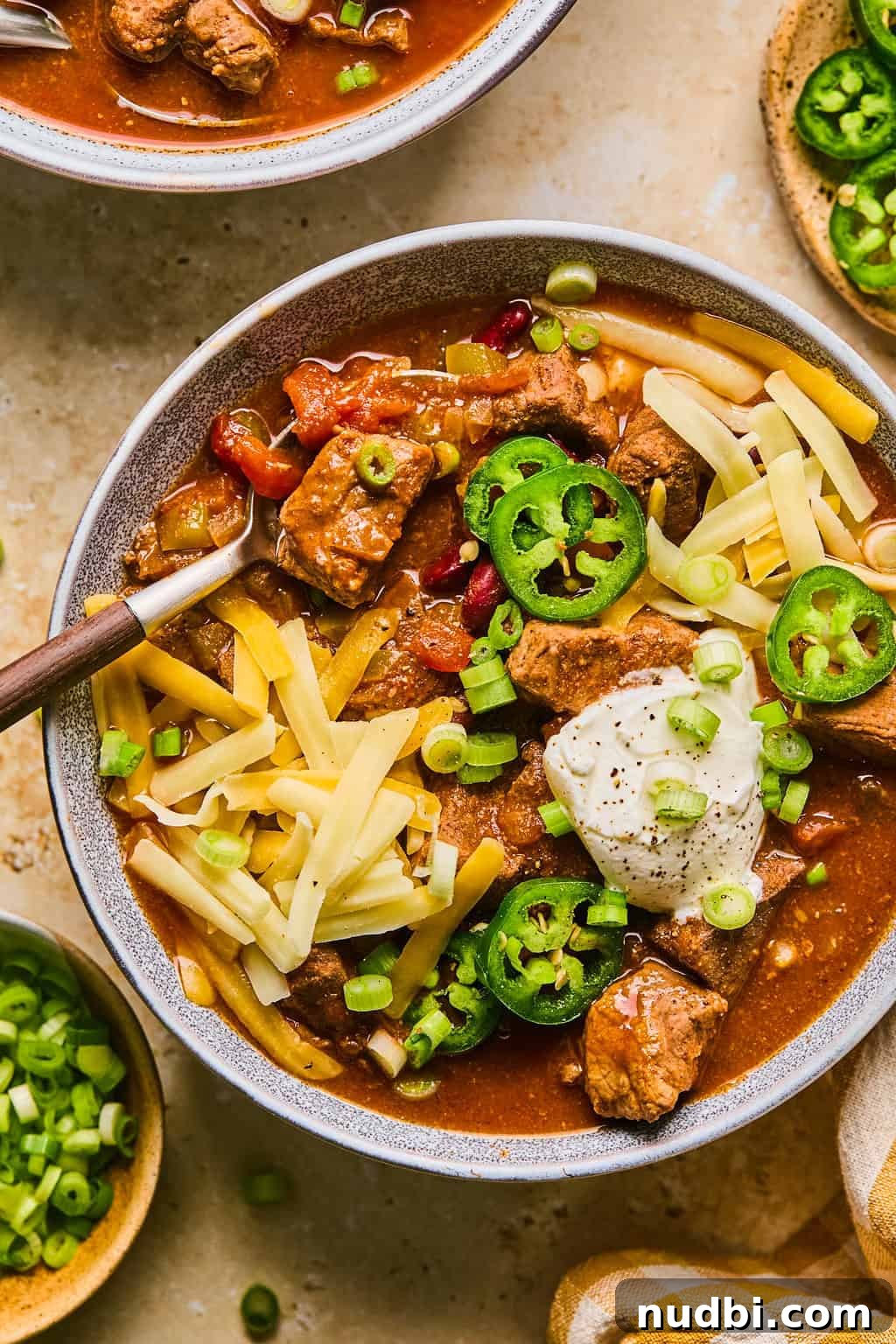 Slow Cooker Beef Brisket Chili Recipe for Tender, Smoky Flavor 2 Bowl of beef brisket chili topped with cheese, sour cream, green onions etc.
