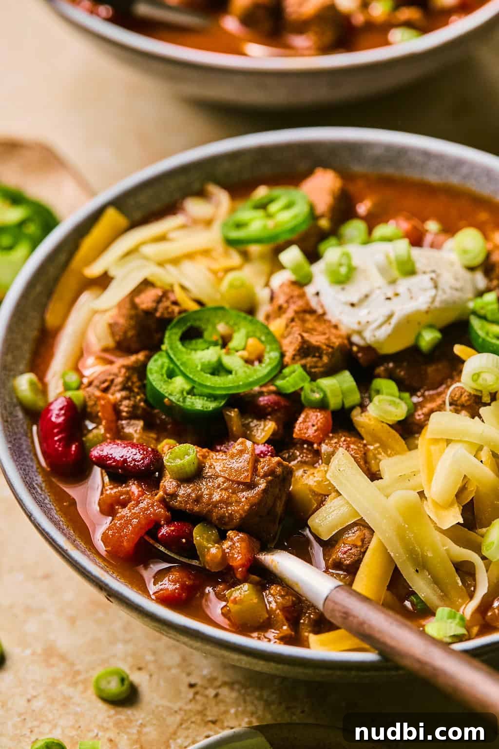 Slow Cooker Beef Brisket Chili Recipe for Tender, Smoky Flavor 12 Bowl of chili with spoon scooping into it and topped with cheese and other ingredients.