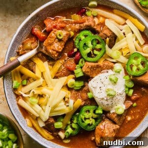 Slow Cooker Beef Brisket Chili Recipe for Tender, Smoky Flavor 13 Bowl of chili with brisket, shredded cheese, sour cream and spoon scooping up a spoonful.