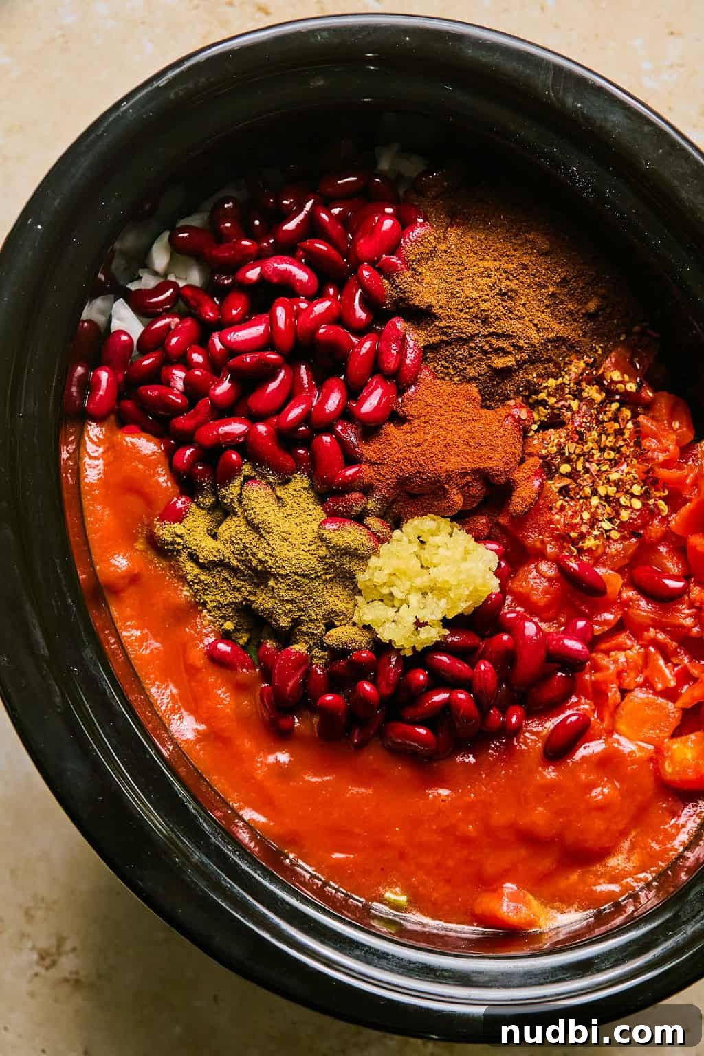 Slow Cooker Beef Brisket Chili Recipe for Tender, Smoky Flavor 7 Beans, garlic, spices and tomatoes over top of other ingredients in crockpot.