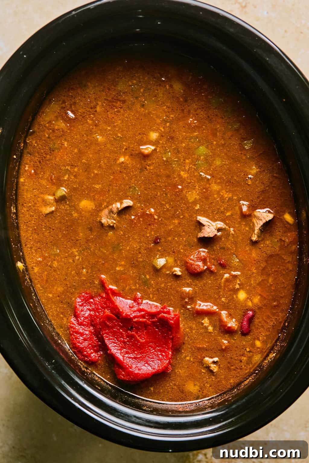 Slow Cooker Beef Brisket Chili Recipe for Tender, Smoky Flavor 9 Beef brisket chili cooked and then tomato paste being added to the pot.