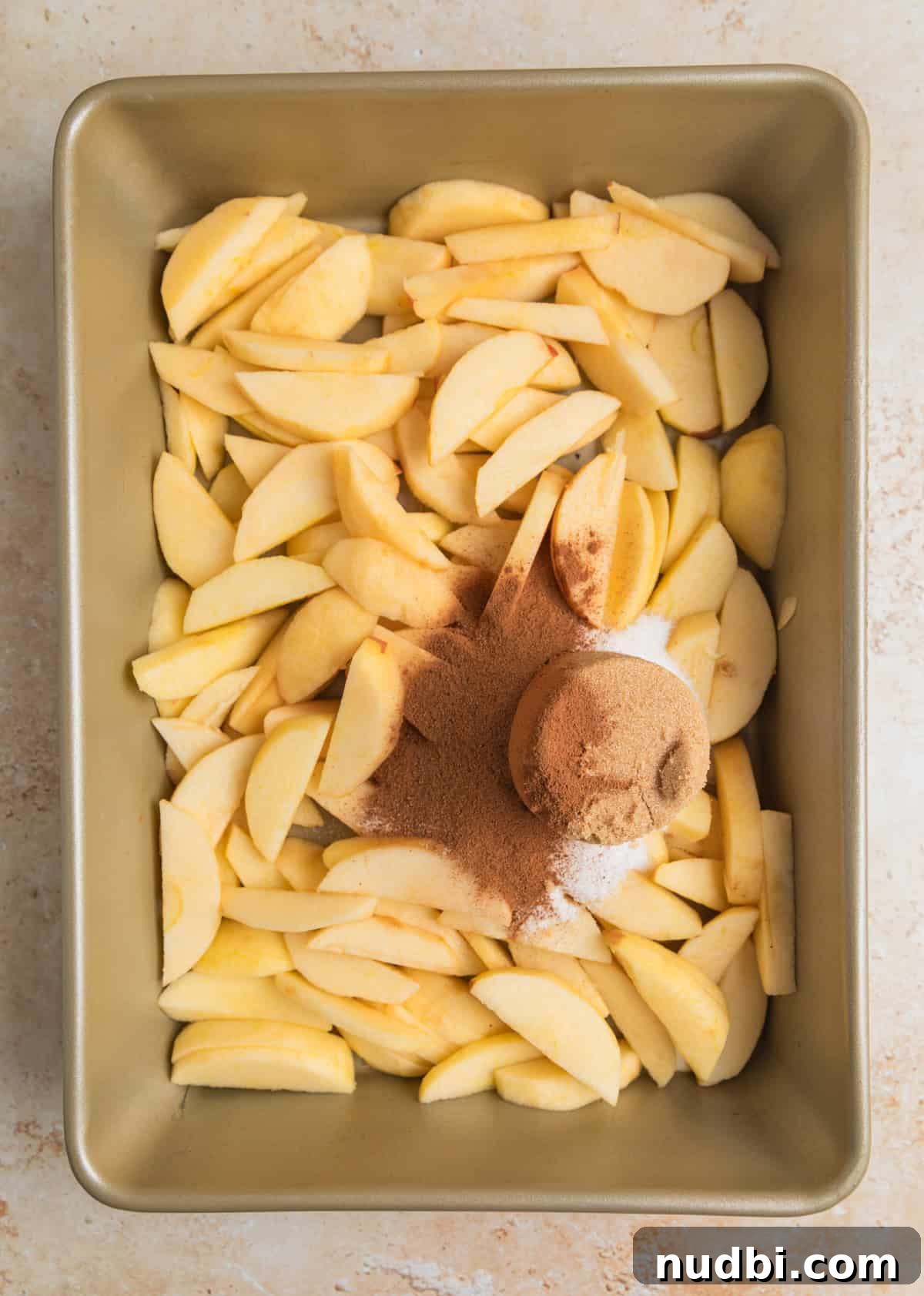 Classic Apple Dump Cake Recipe: Quick Homemade Comfort Dessert 5 Cinnamon, brown sugar, and white sugar over top of sliced apples in pan.