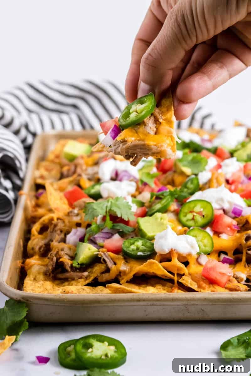 Ultimate Pulled Pork Nachos Recipe for Game Day Crowd 6 Chip with cheese and jalapeno in front of sheet pan.