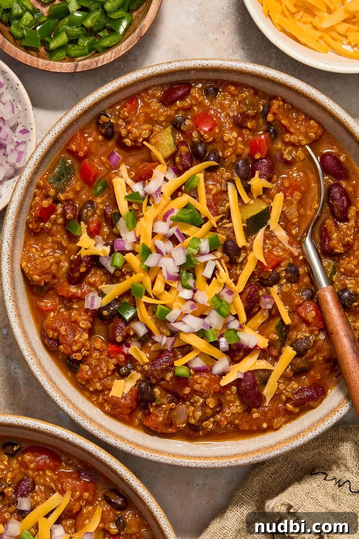 Hearty Pumpkin Quinoa Chili Recipe for Fall Nights 3 Bowl of pumpkin chili recipe topped with cheese, onion and chopped jalapeño.