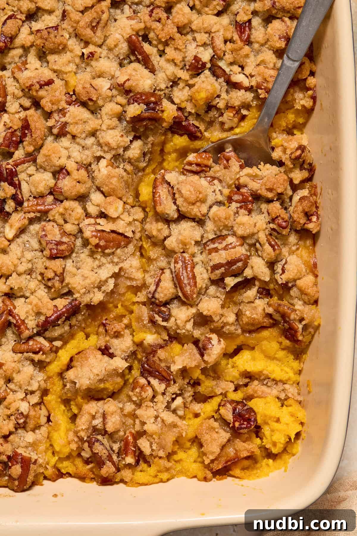 Creamy Butternut Squash Casserole with Sage and Parmesan 9 Serving spoon scooping into pecan crumble topped squash mixture in baking pan.
