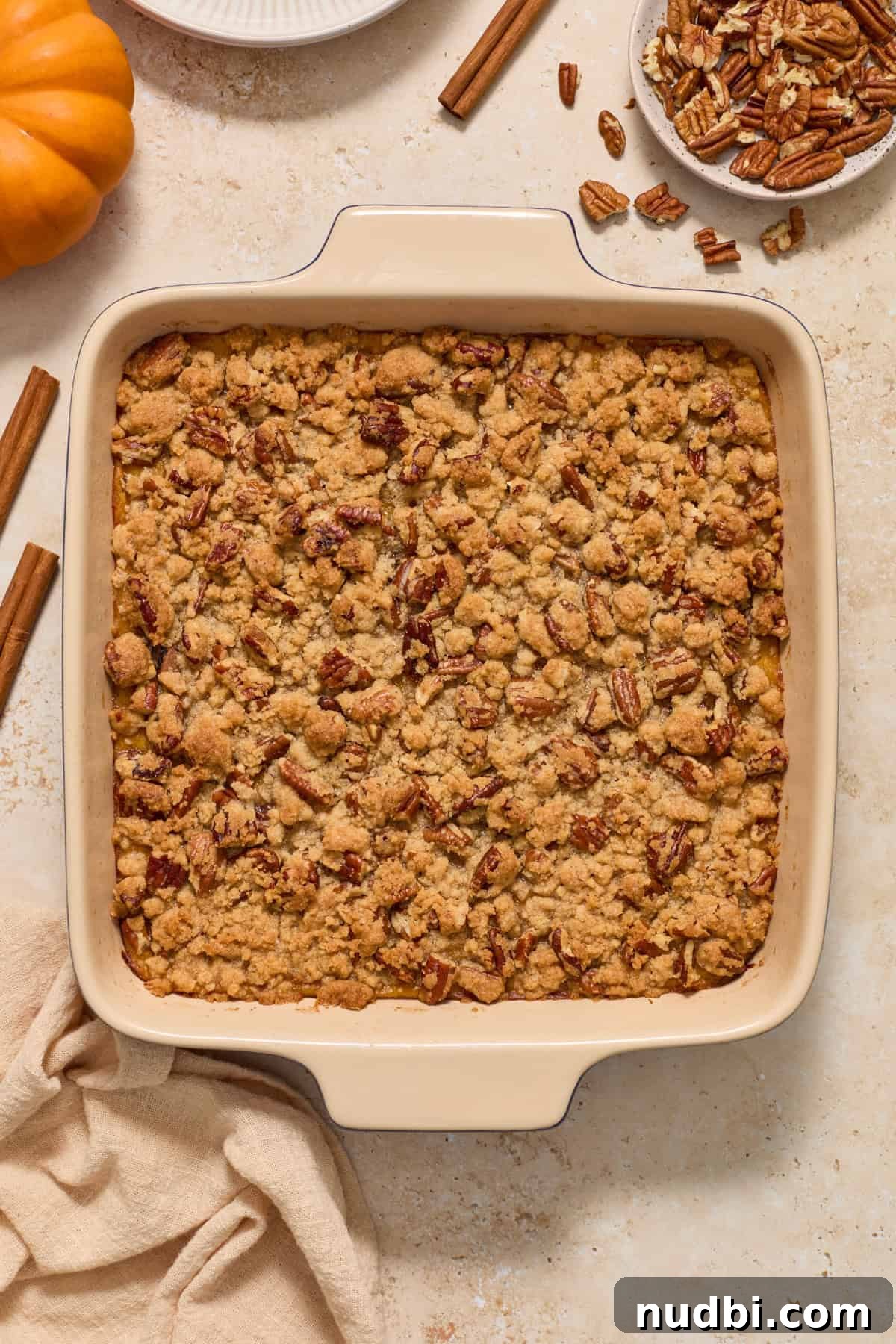 Creamy Butternut Squash Casserole with Sage and Parmesan 8 Baked crumble topped squash casserole with linen, pumpkin, cinnamon stick and other ingredients surrounding.