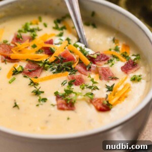 Creamy Instant Pot Potato and Leek Soup Recipe 9 Beige bowl with potato soup topped with bacon, cheese, chives and sour cream.