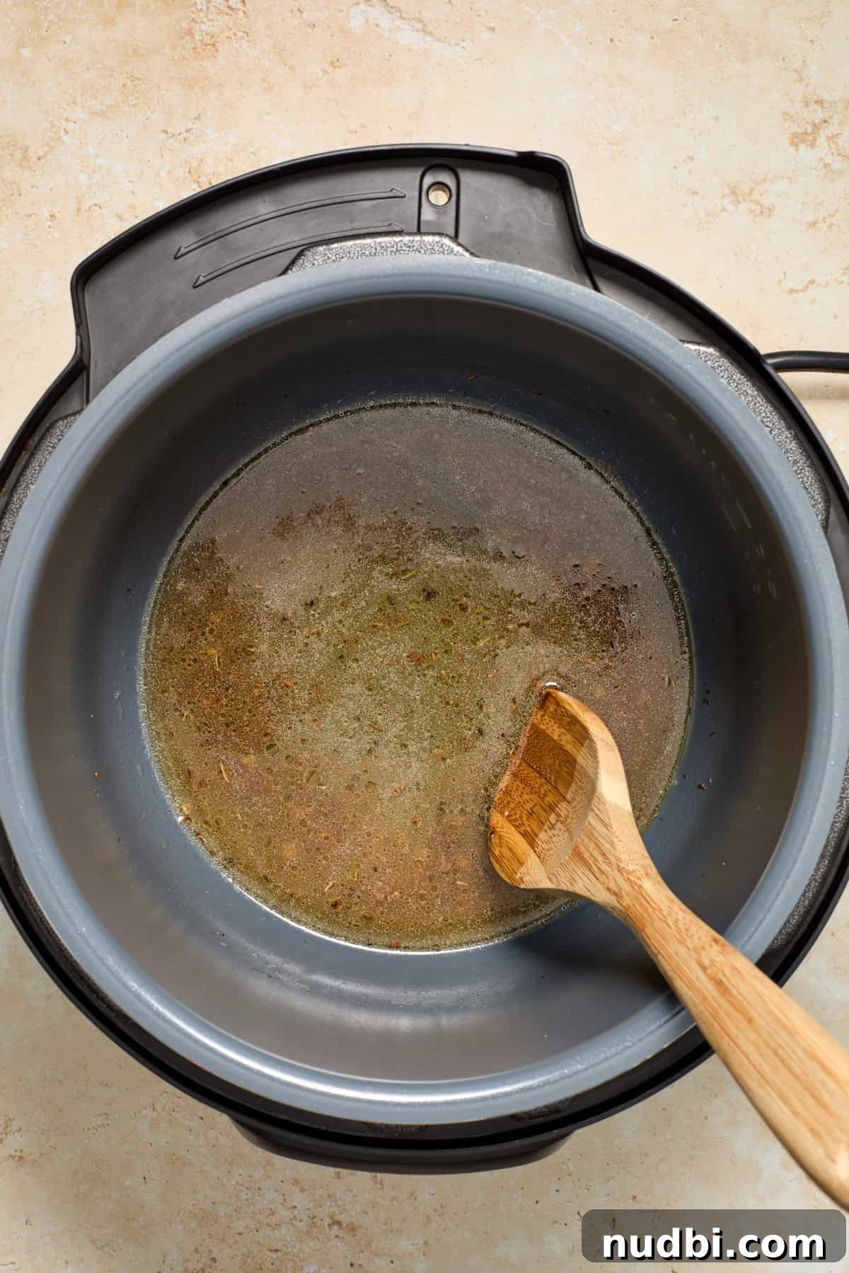 Juicy Instant Pot Pork Tenderloin Recipe for Quick Dinners 8 Deglazed instant pot with broth and wooden spoon.