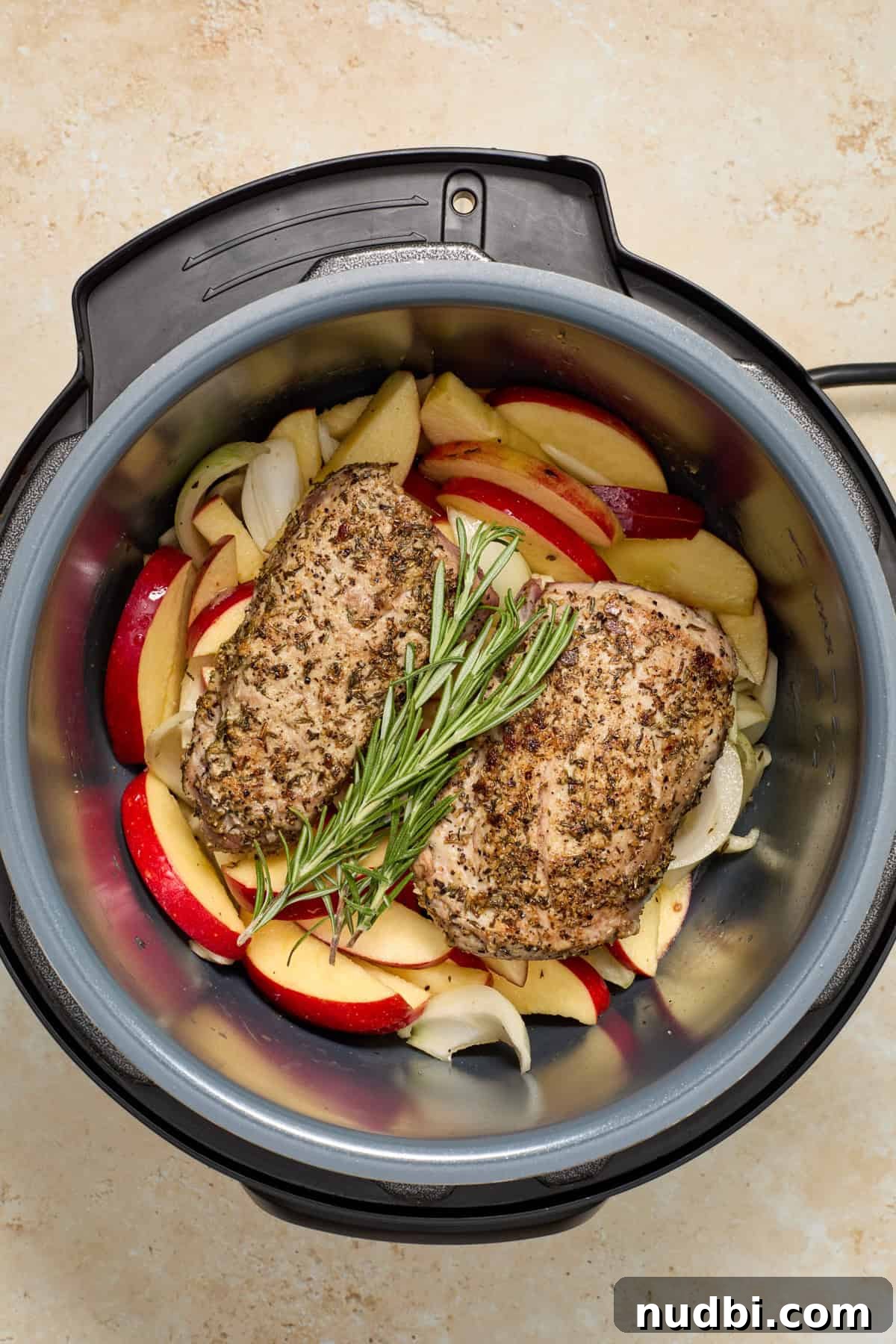 Juicy Instant Pot Pork Tenderloin Recipe for Quick Dinners 10 Seared pork tenderloin on top of apples and onions with rosemary sprig in pressure cooker.
