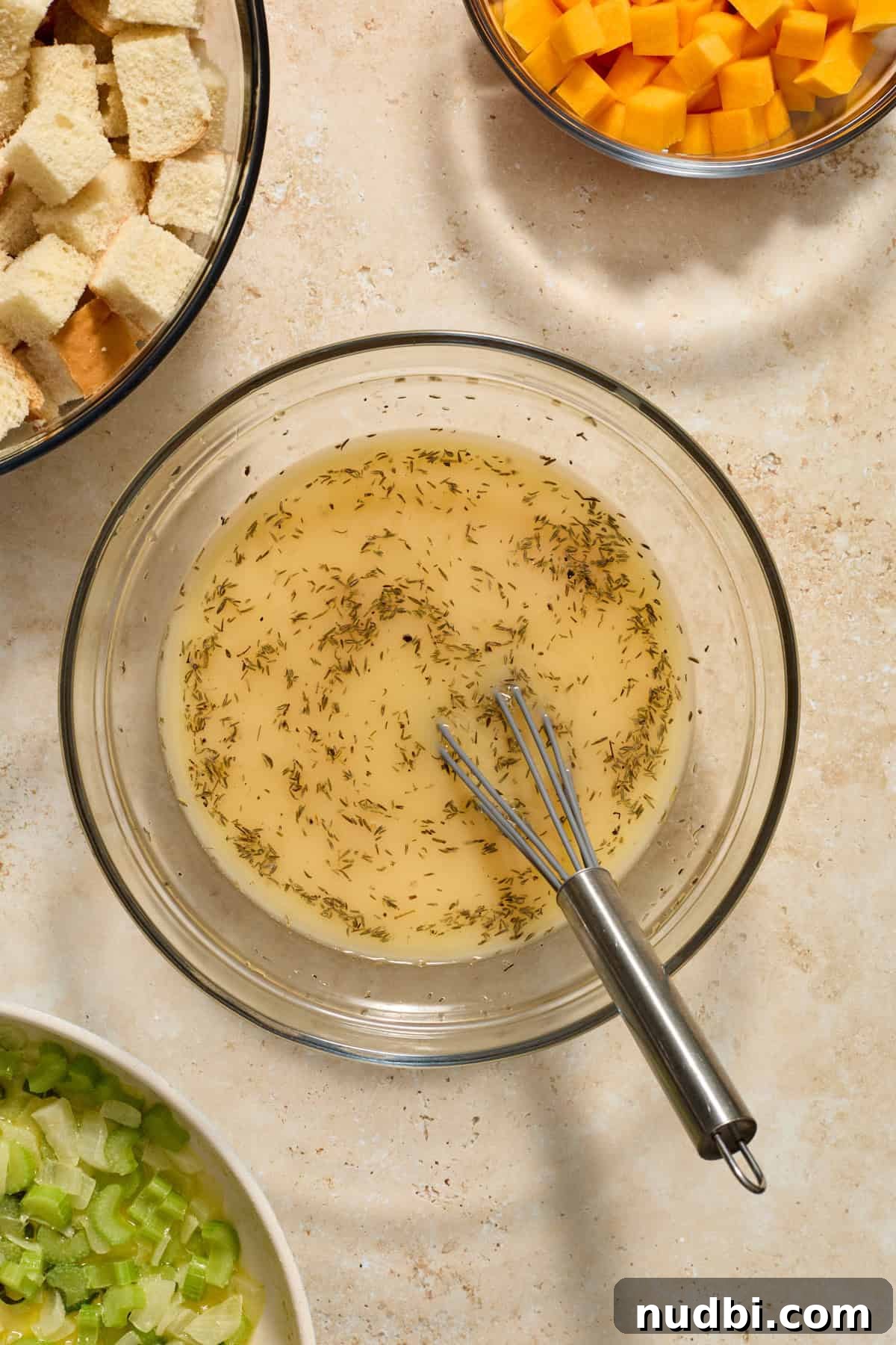 Savory Butternut Squash Stuffing Recipe for Holiday Dinners 5 Whisked broth and herb mixture in glass mixing bowl with whisk in bowl.