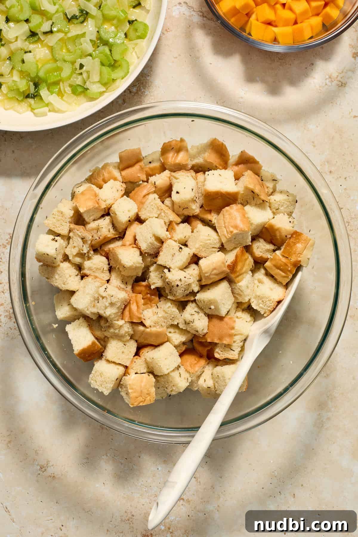 Savory Butternut Squash Stuffing Recipe for Holiday Dinners 6 Bread cubes in glass bowl with spatula and cooked veggies in skillet as well as squash cubes in bowl.