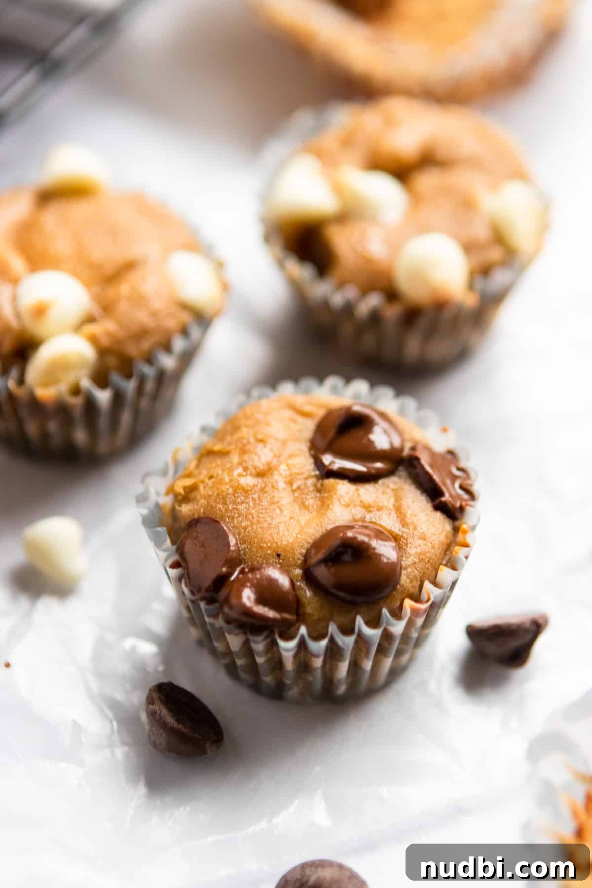 Peanut Butter Banana Mini Muffins (Flourless, Gluten-Free) 6 Mini muffins with chocolate chips melted on top laying on top of parchment.
