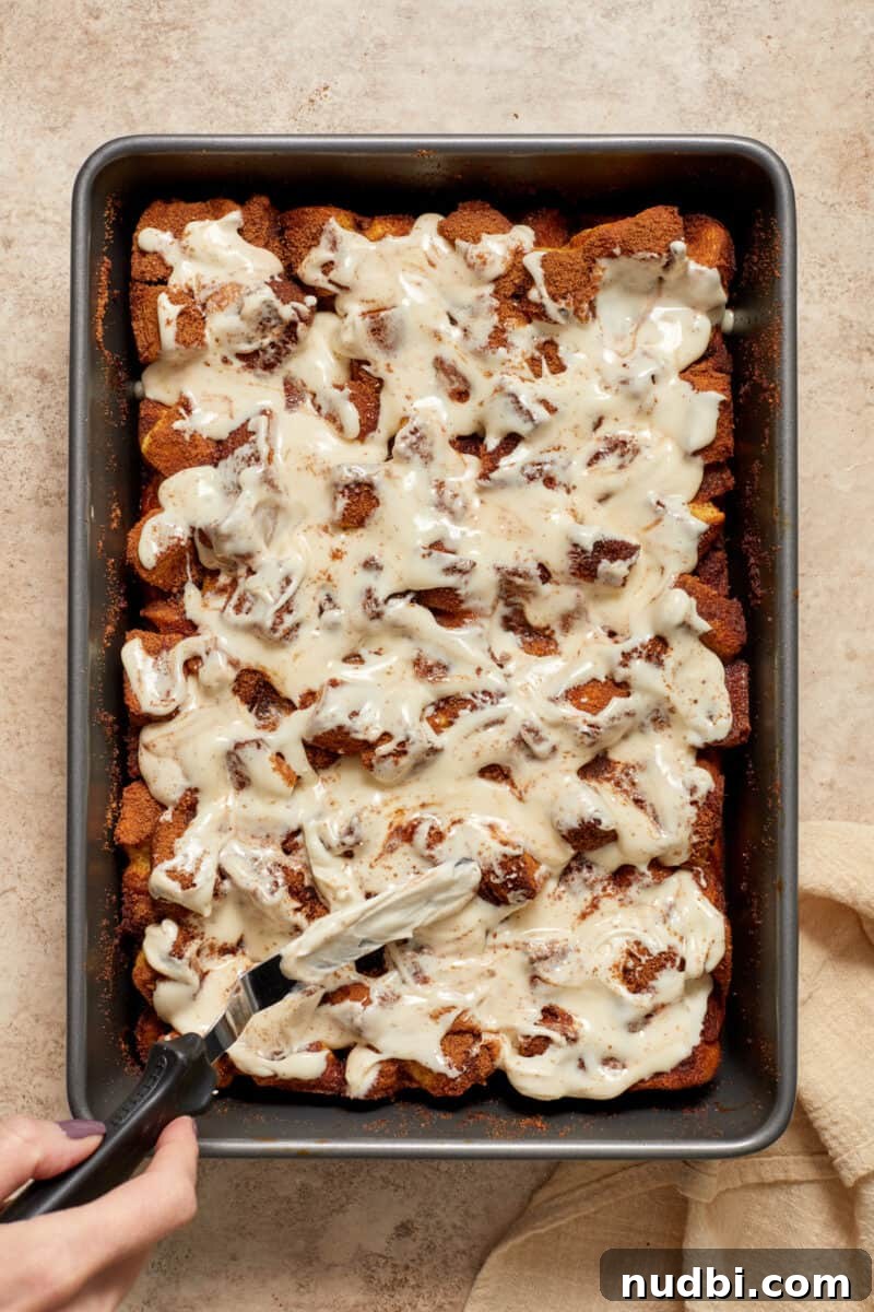 Cinnamon Roll Baked French Toast Recipe for Brunch 11 Cinnamon French toast bake in pan with icing being spread over top.