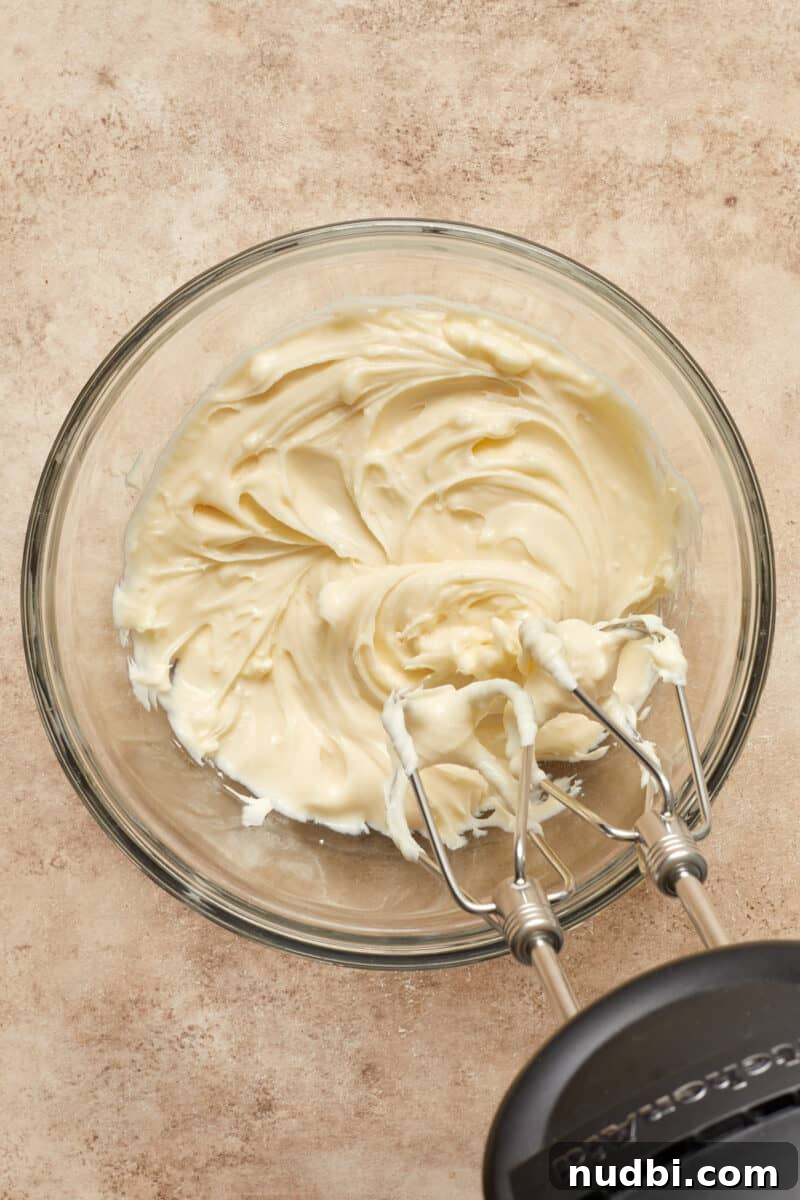 Cinnamon Roll Baked French Toast Recipe for Brunch 10 Cream cheese frosting in glass mixing bowl with electric hand mixer to the side.