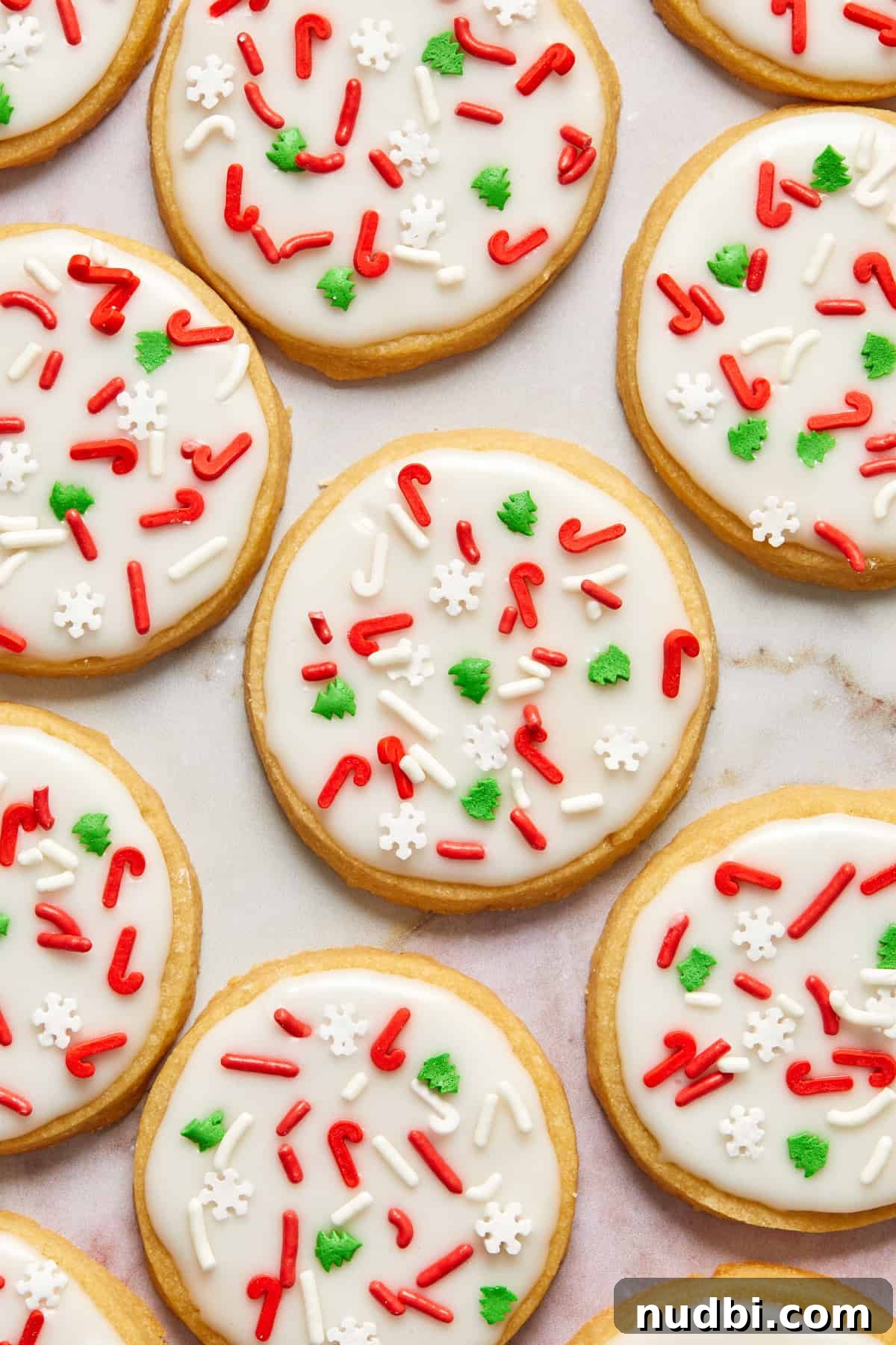 Classic Christmas Shortbread Cookies Recipe for the Holidays 2 Christmas shortbread cookies with white icing and red and green holiday sprinkles arranged on counter.