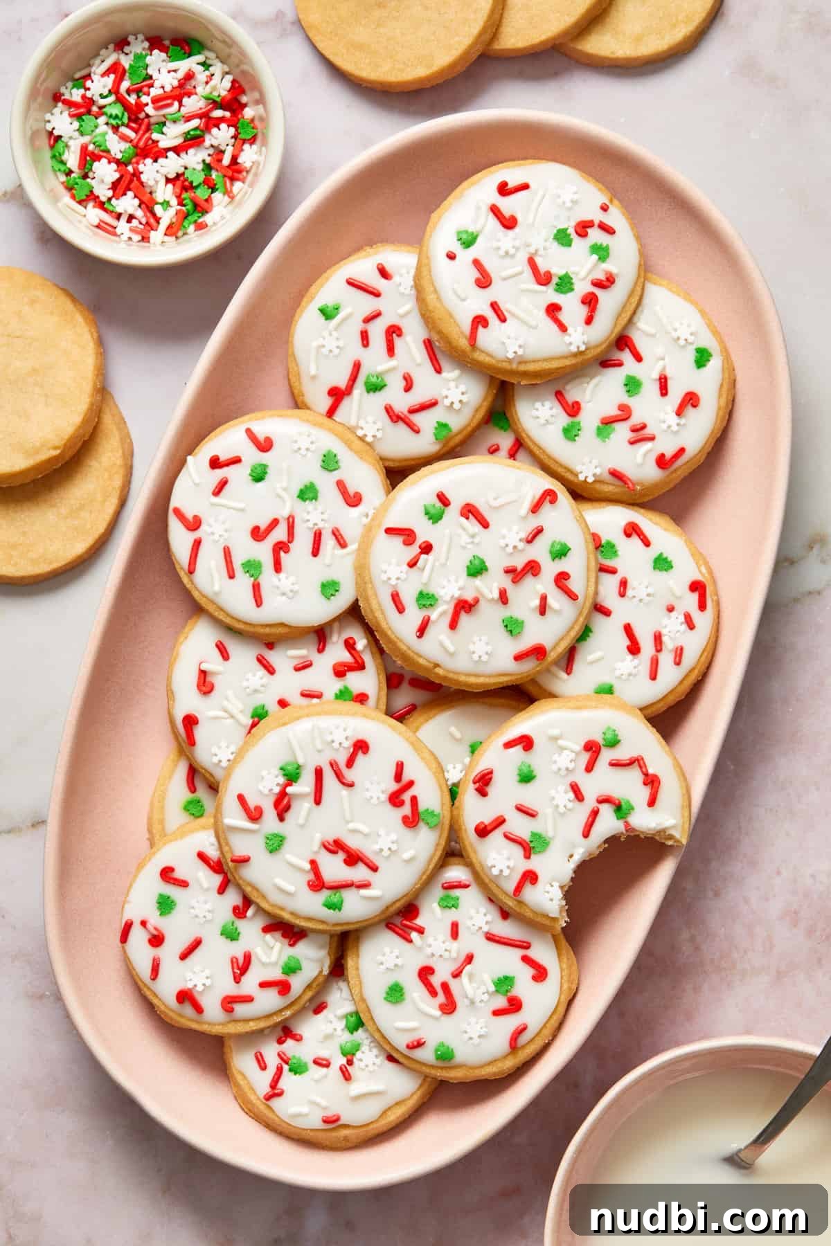 Classic Christmas Shortbread Cookies Recipe for the Holidays 12 Pink dish filled with iced shortbread cookies with red and green sprinkles.