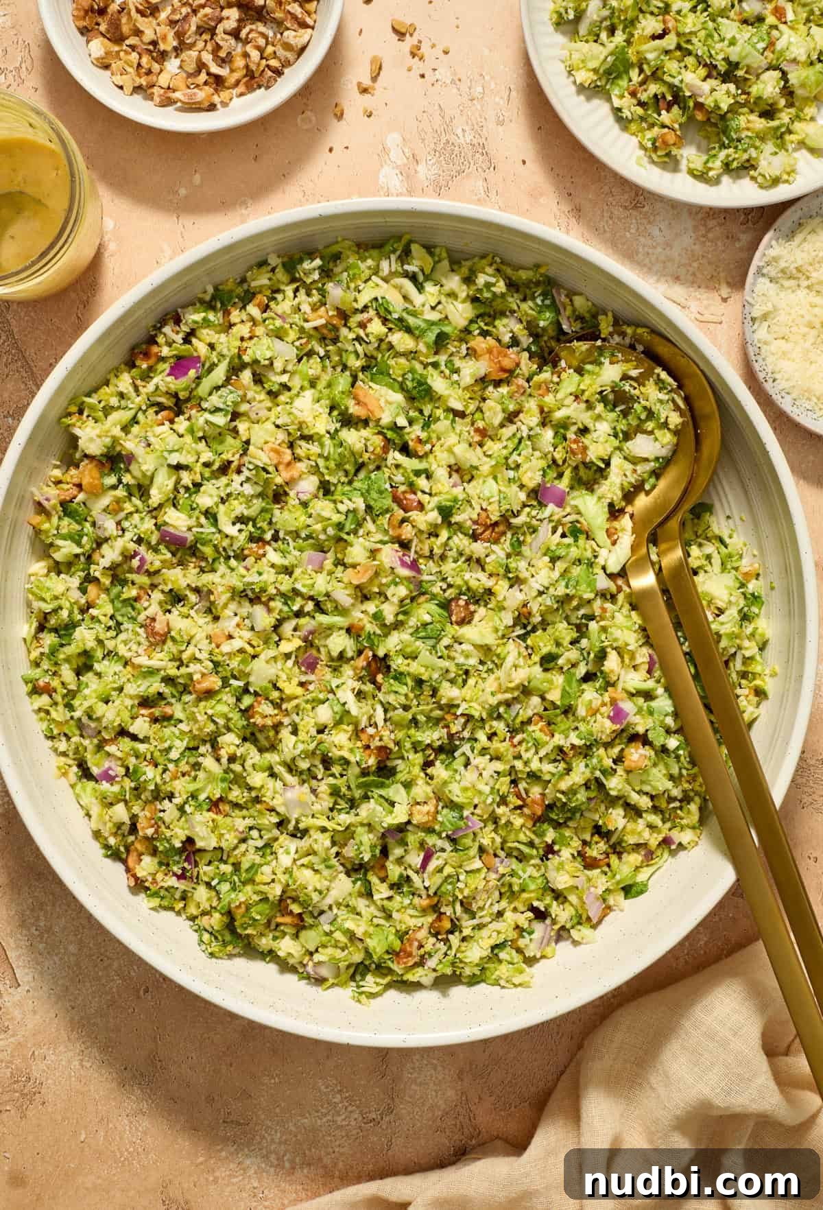 Crisp Shaved Brussels Sprout Salad with Lemon Parmesan Dressing 2 Shaved brussel sprout salad in serving bowl with serving utensils propped in the salad bowl.