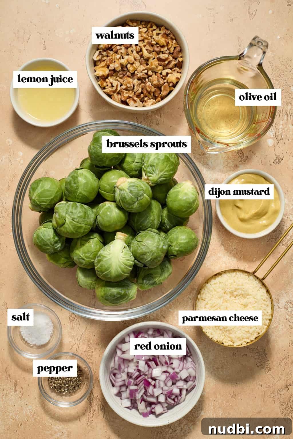 Crisp Shaved Brussels Sprout Salad with Lemon Parmesan Dressing 3 Brussels sprouts in bowl, walnuts, chopped onion, parmesan and other ingredients labeled on surface.