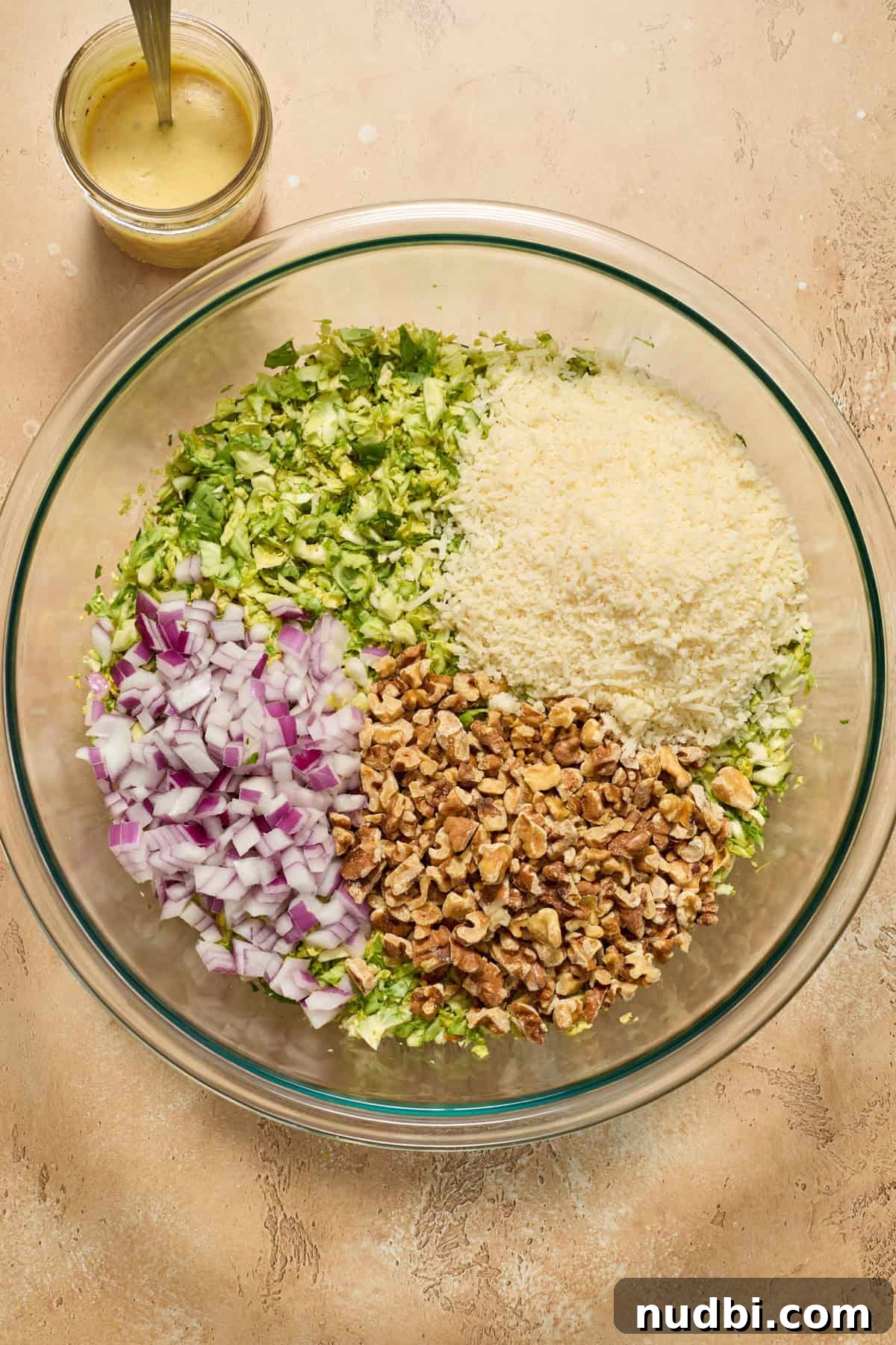 Crisp Shaved Brussels Sprout Salad with Lemon Parmesan Dressing 6 Shredded brussels sprouts in large bowl with red onion, walnut pieces and shredded parmesan before mixing.