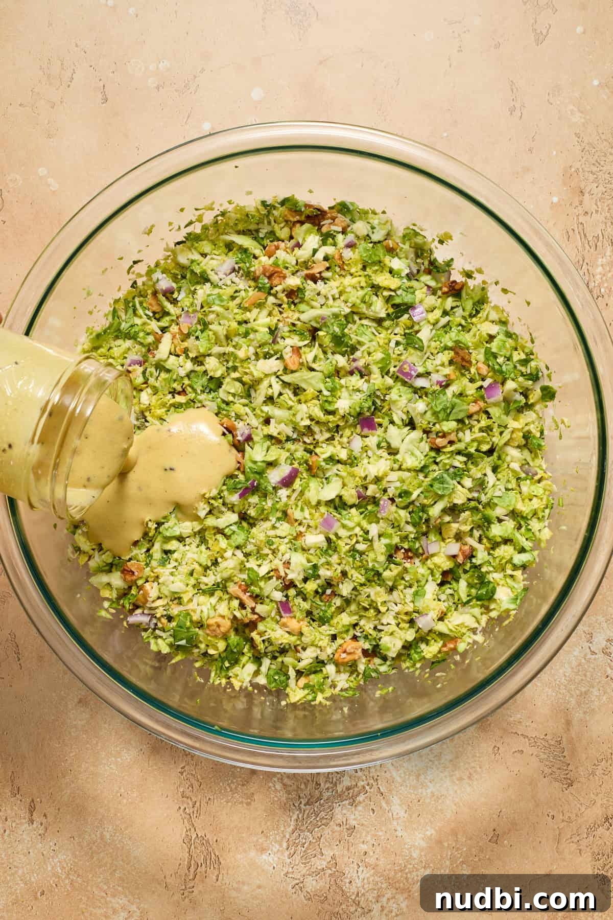 Crisp Shaved Brussels Sprout Salad with Lemon Parmesan Dressing 9 Dressing being poured over shredded brussels sprouts salad before tossing.