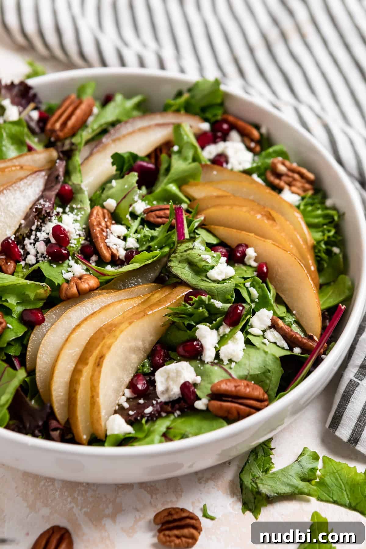 Warm Roasted Pear Salad with Goat Cheese and Candied Pecans 2 White salad bowl with spring greens, roasted pears, pomegranates, goat cheese and pecans.