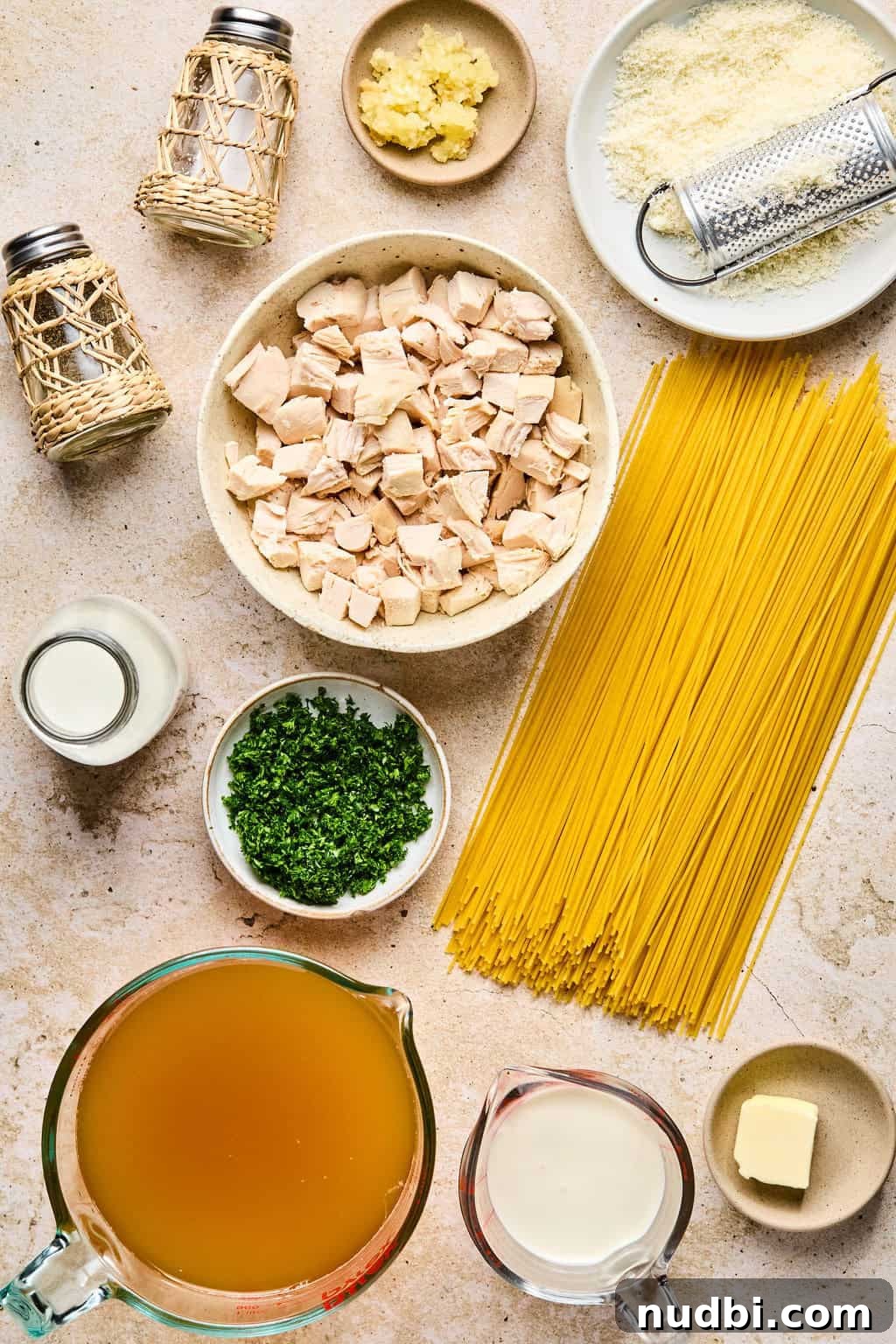 Creamy Chicken Alfredo Dinner Recipe in 30 Minutes 4 Pasta, chicken cubed, broth, parsley and other ingredients arranged on surface.