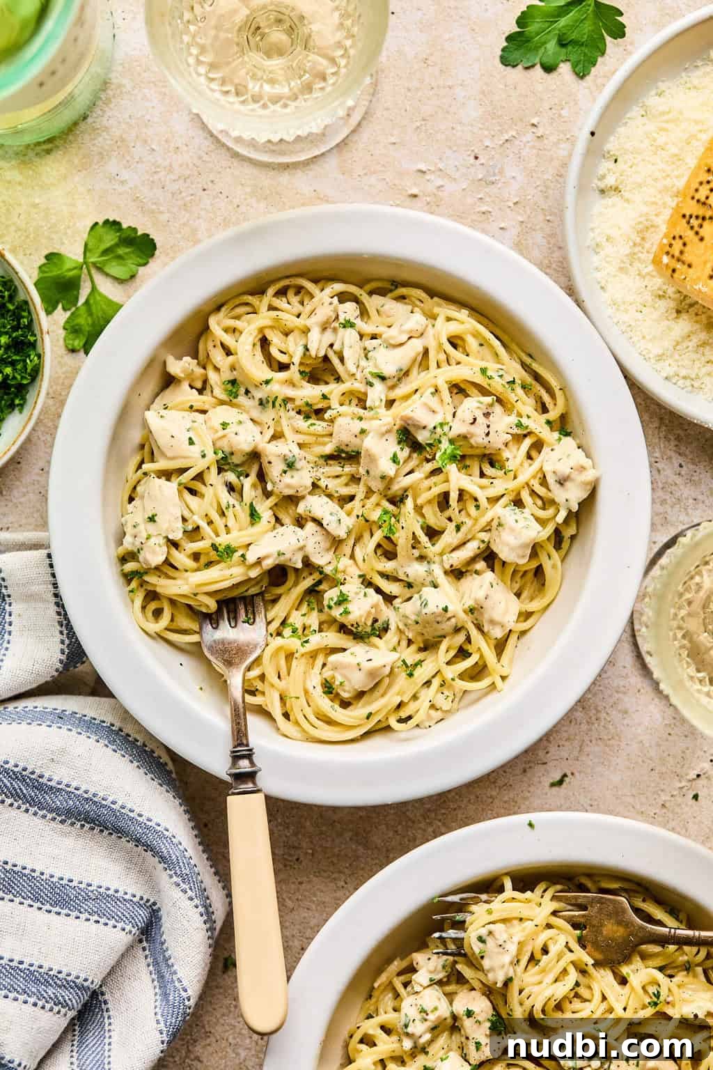 Creamy Chicken Alfredo Dinner Recipe in 30 Minutes 7 Bowl of chicken Alfredo with napkin, wine, parsley and other ingredients surrounding it.