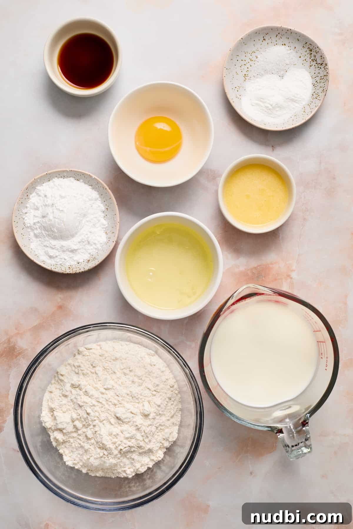 Flour, milk, eggs, vanilla and other ingredients to arranged on surface.