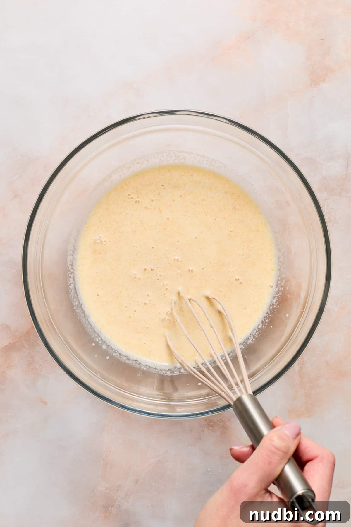 Eggs and wet ingredients whisked together in glass mixing bowl.