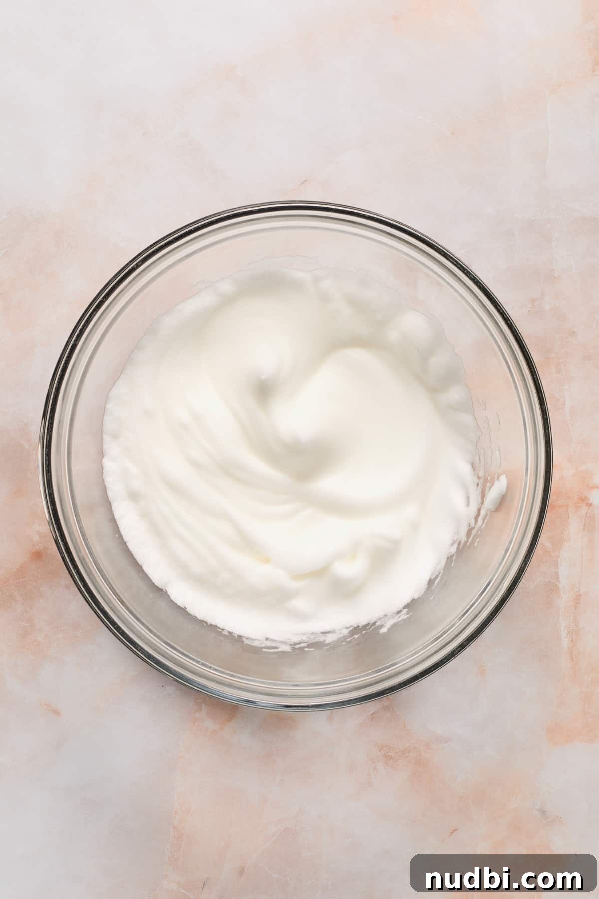 Egg whites beaten to thick stiff peaks in glass bowl.