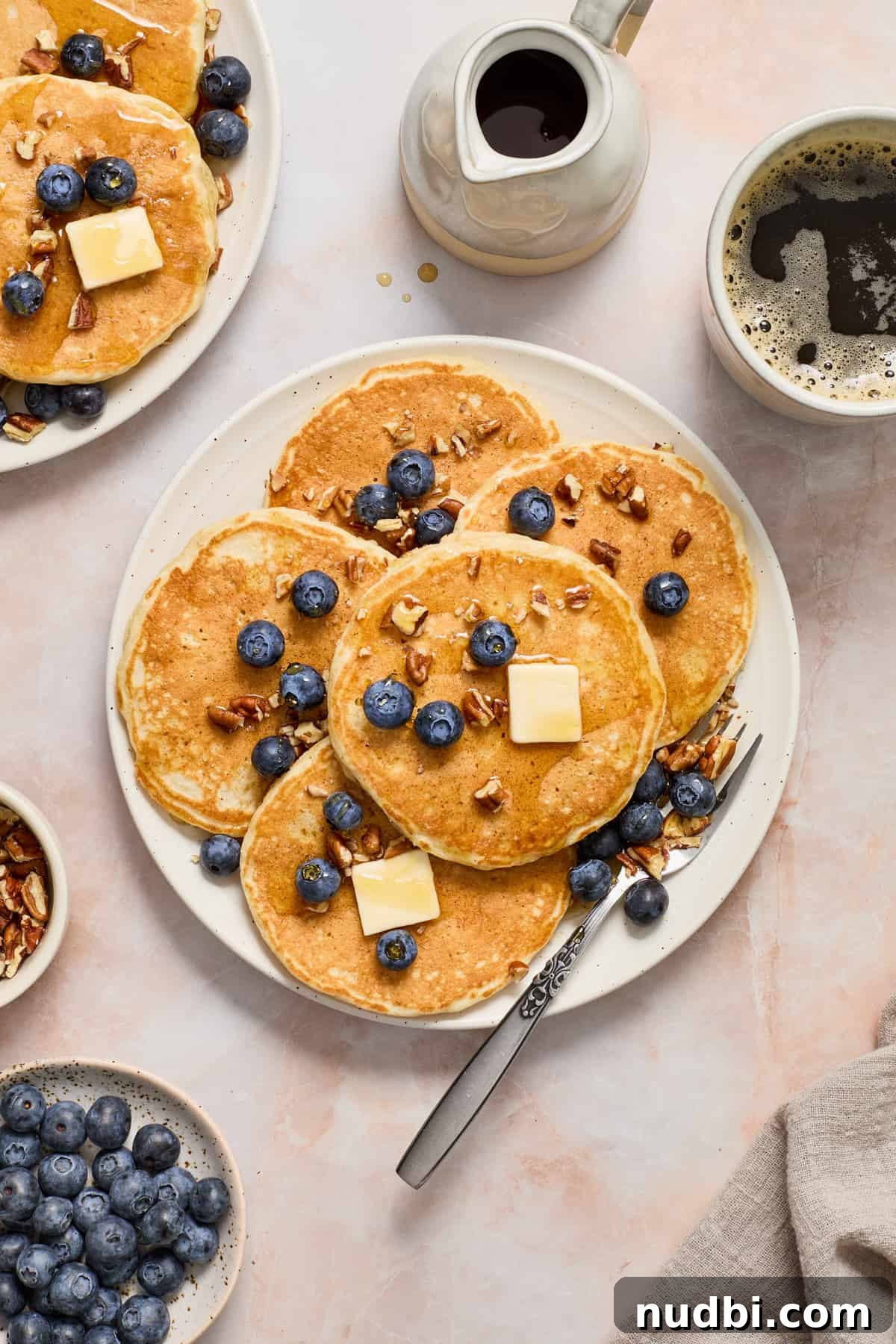 Fluffy egg white pancakes on white plate with fork and topped with butter and blueberries.