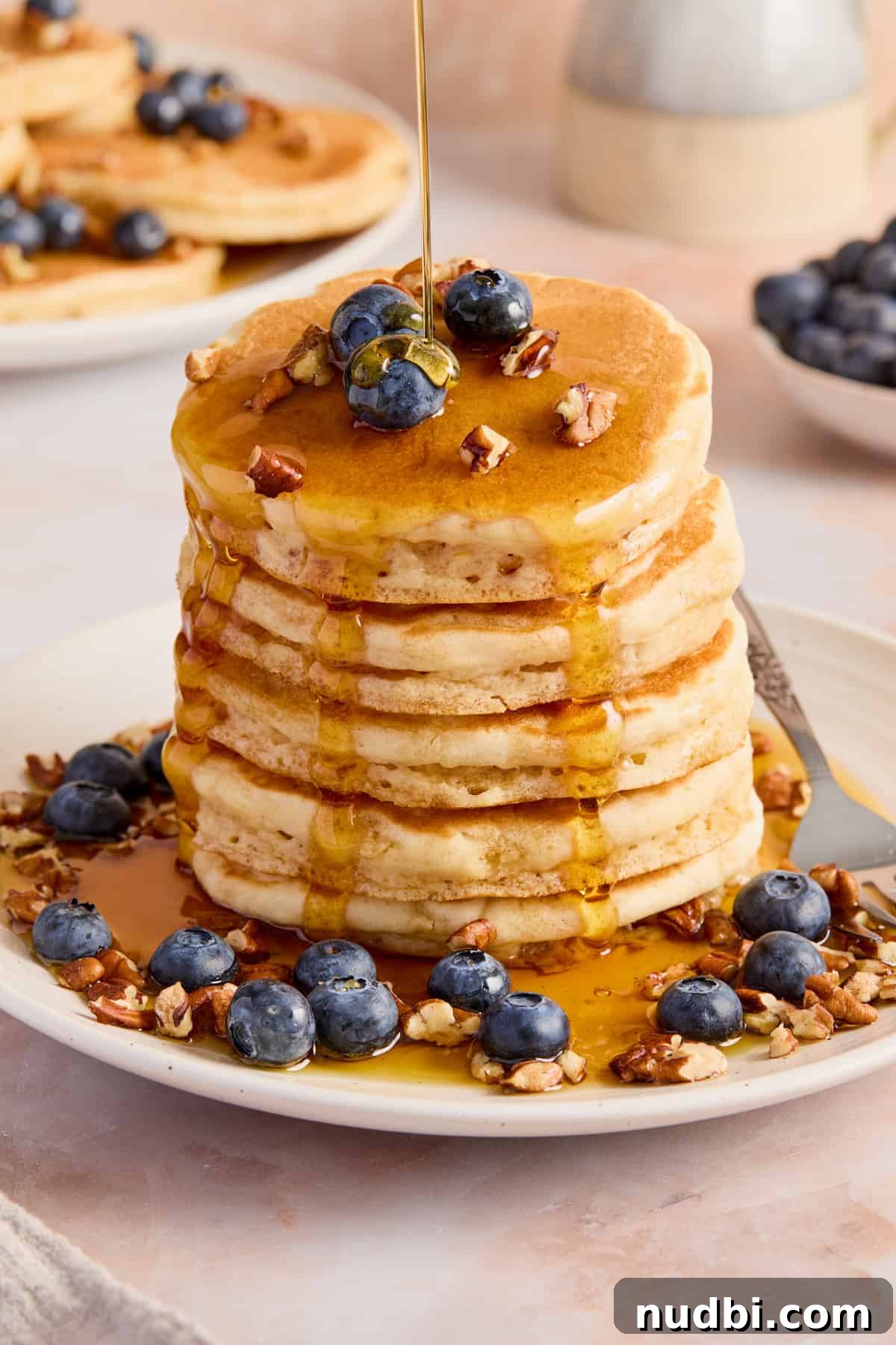 Stack of pancakes on plate with blueberries and pecans.