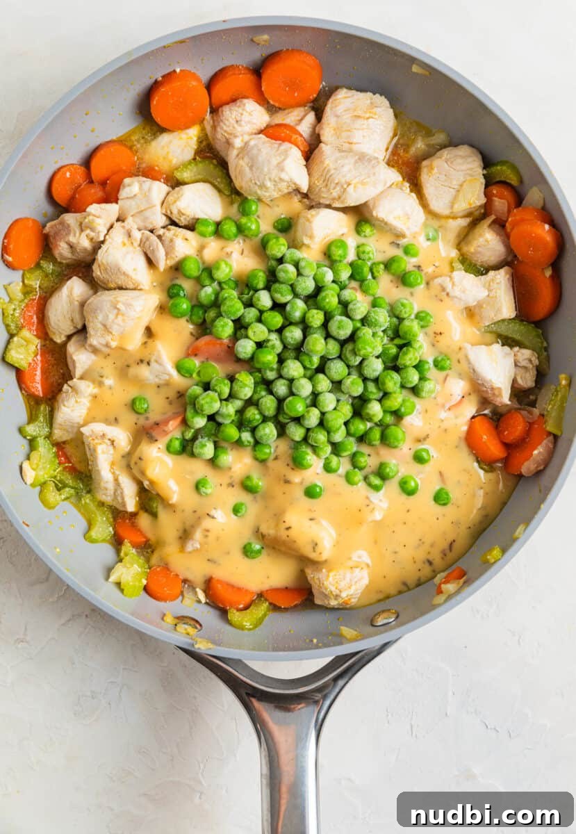 One-Pan Chicken and Biscuits Skillet Recipe 6 Peas and chicken soup mixture added to skillet with cooked chicken and vegetables.