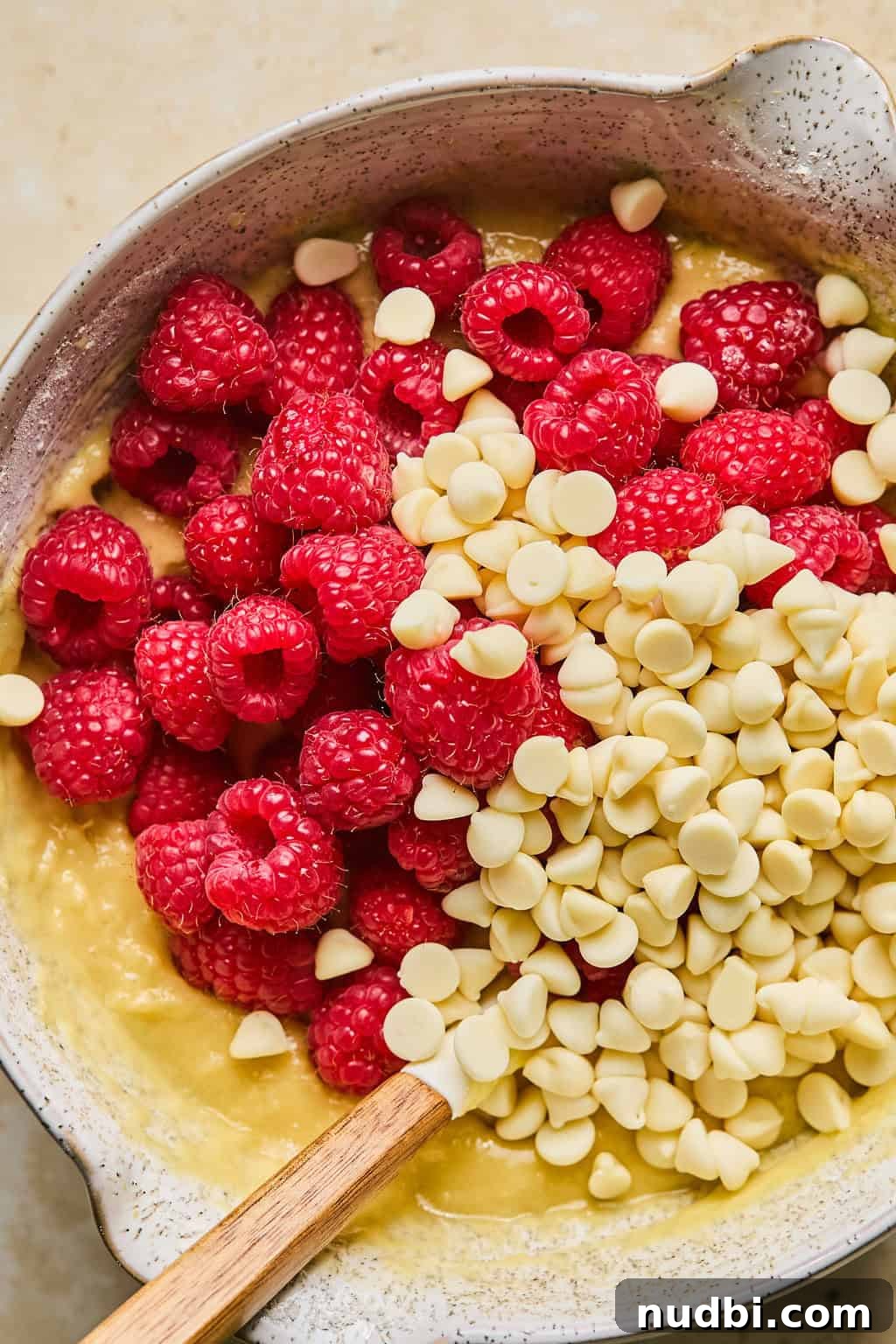 White Chocolate Raspberry Muffins Recipe — Moist, Fruity Treat 8 Raspberries and white chocolate chips added to mixing bowl with batter.