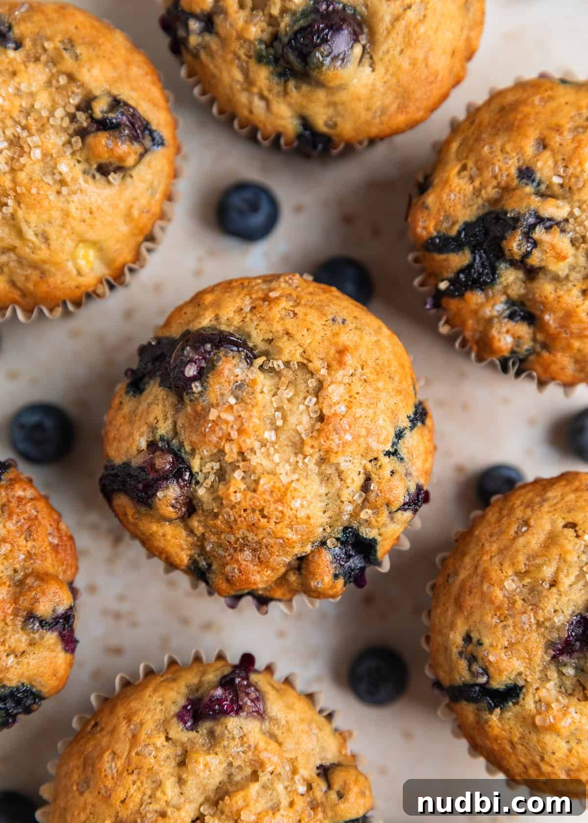 Moist Banana Blueberry Muffins with a Crunchy Streusel 12 Overhead view of baked banana blueberry muffins on surface with coarse sugar and berries surrounding.