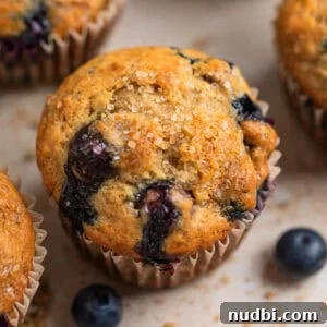 Moist Banana Blueberry Muffins with a Crunchy Streusel 13 Blueberry muffin with coarse sugar on top and crumbs and berries surrounding.