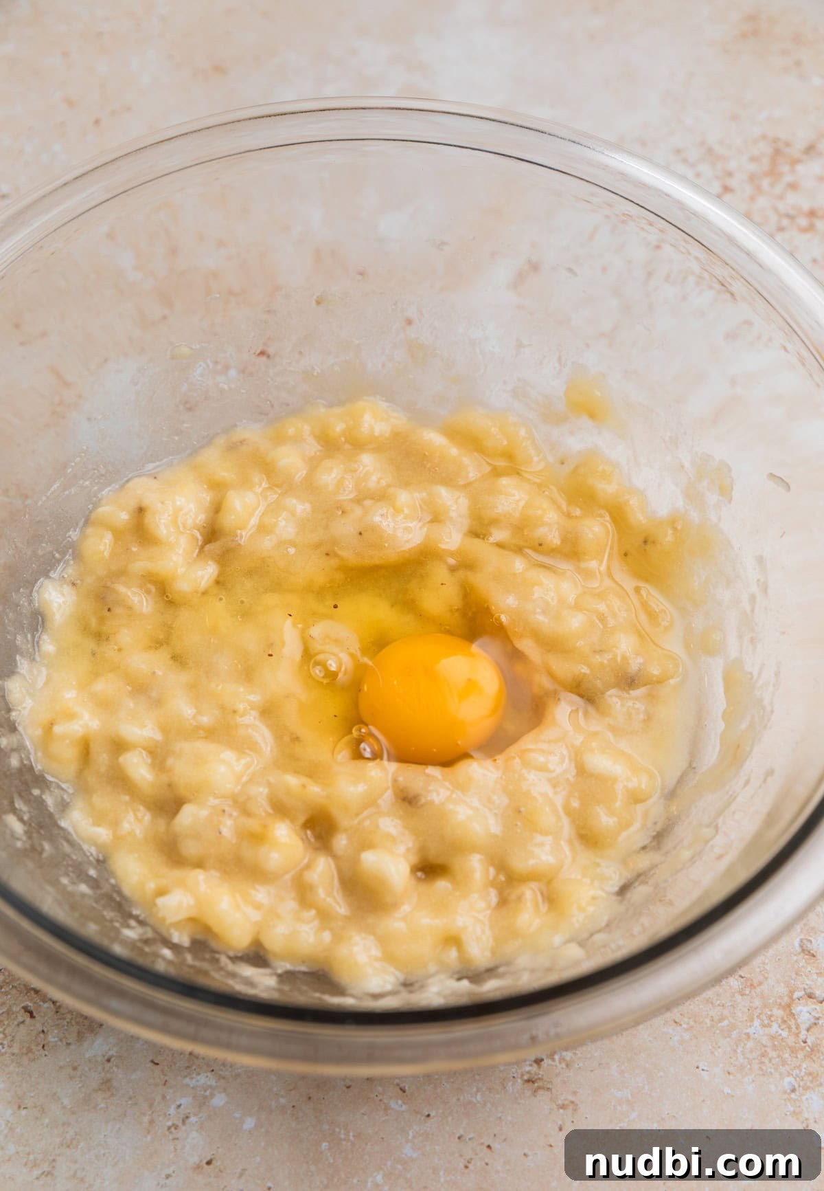 Moist Banana Blueberry Muffins with a Crunchy Streusel 4 Mashed banana in mixing bowl with egg in it before whisking.