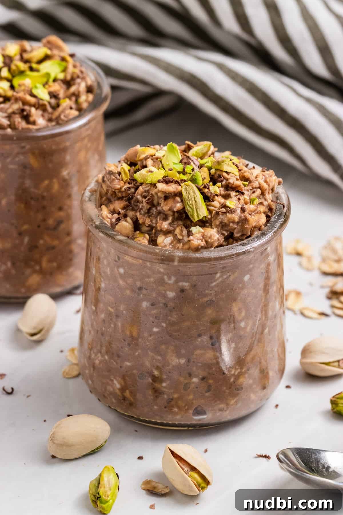 Chocolate Pistachio Overnight Oats Recipe for Creamy Make-Ahead Breakfast 2 Jar of overnight oats with pistachios on top and cracked shells surrounding.