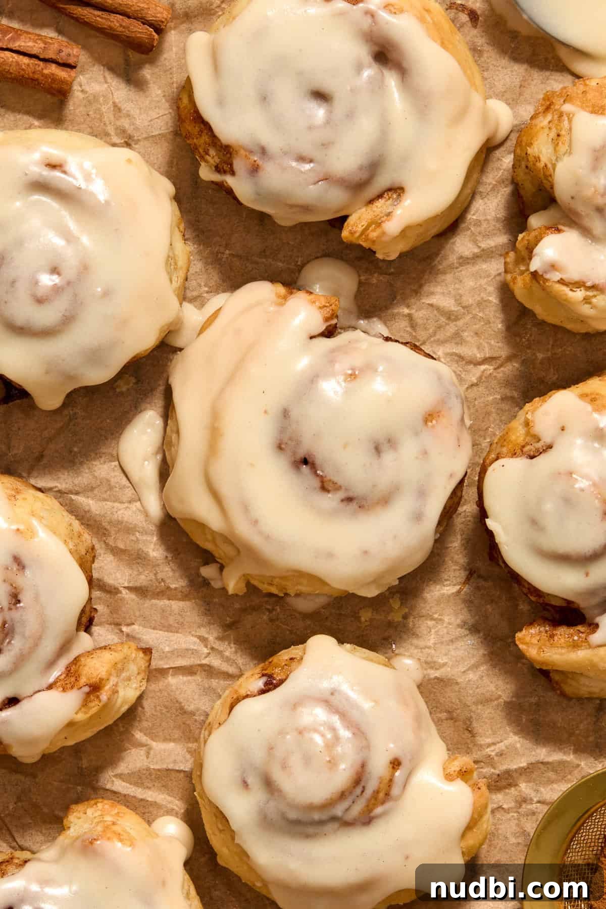 Quick Puff Pastry Cinnamon Rolls with Sticky Cinnamon Glaze 2 Cinnamon rolls with icing on top on parchment.