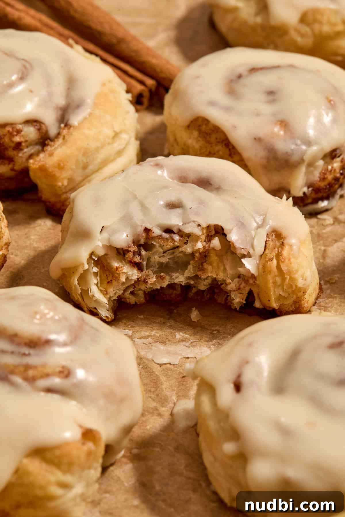 Quick Puff Pastry Cinnamon Rolls with Sticky Cinnamon Glaze 13 Puff pastry cinnamon rolls on parchment with bite taken out of cinnamon roll.