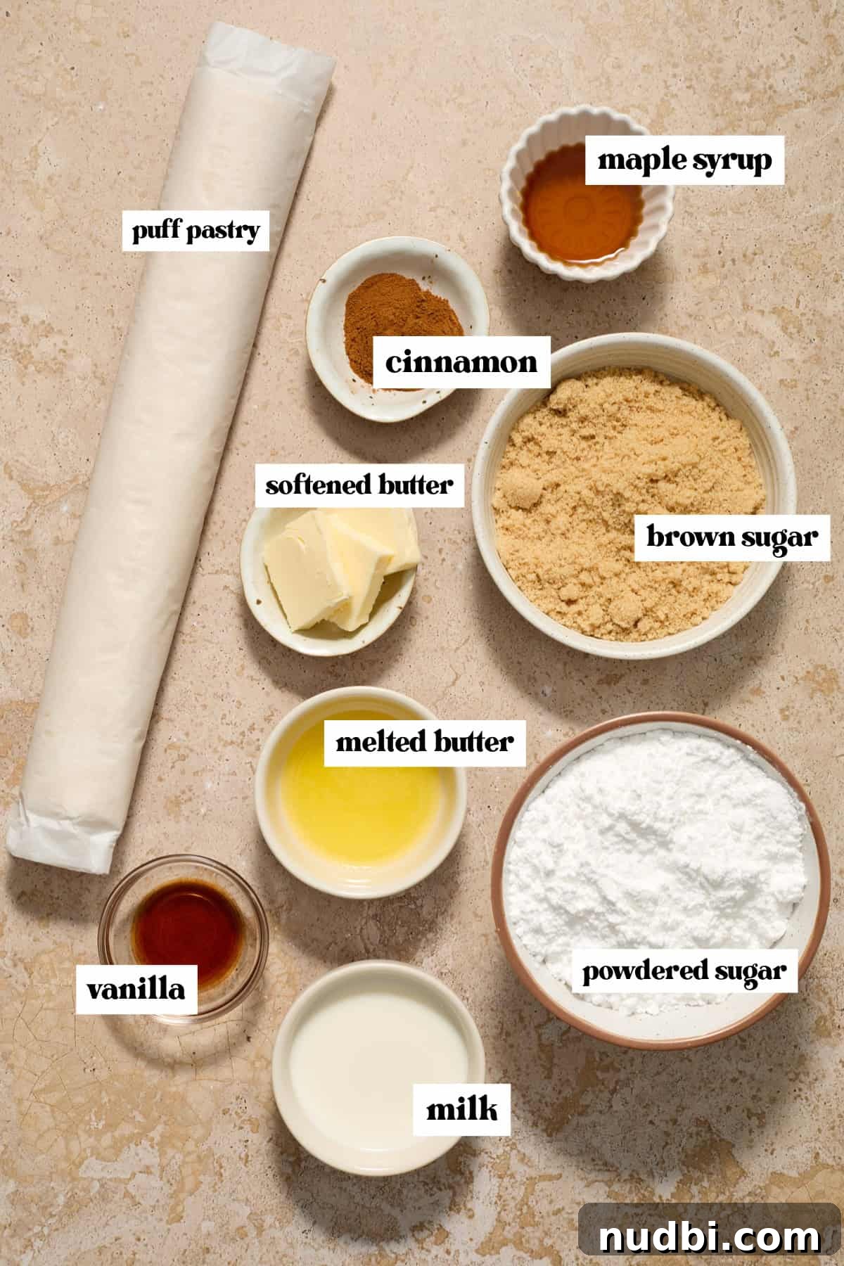 Quick Puff Pastry Cinnamon Rolls with Sticky Cinnamon Glaze 3 Puff pastry roll, brown sugar, cinnamon, butter and other labeled ingredients on surface.