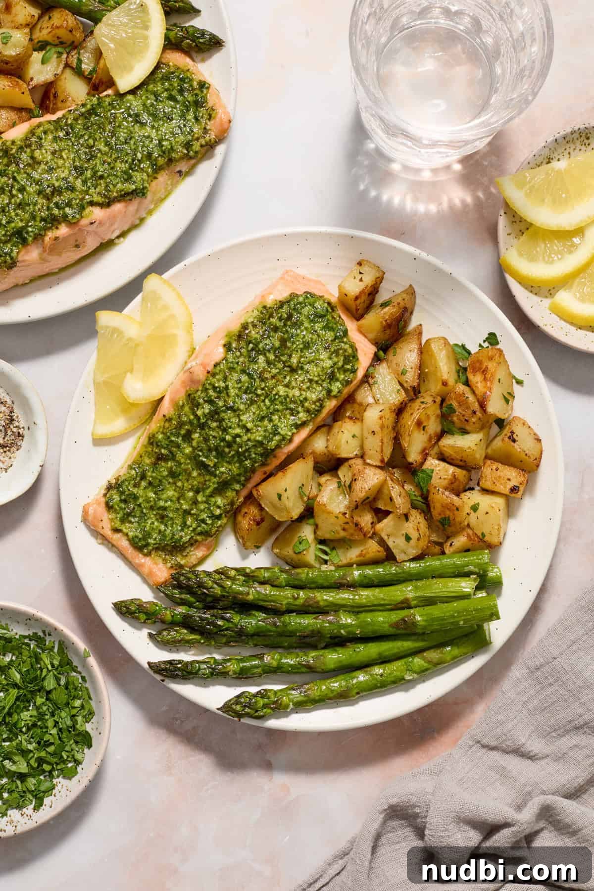 Pesto Salmon Sheet-Pan Dinner with Roasted Veggies 2 Pesto covered salmon on white plate with parmesan potatoes, asparagus and lemon slices.