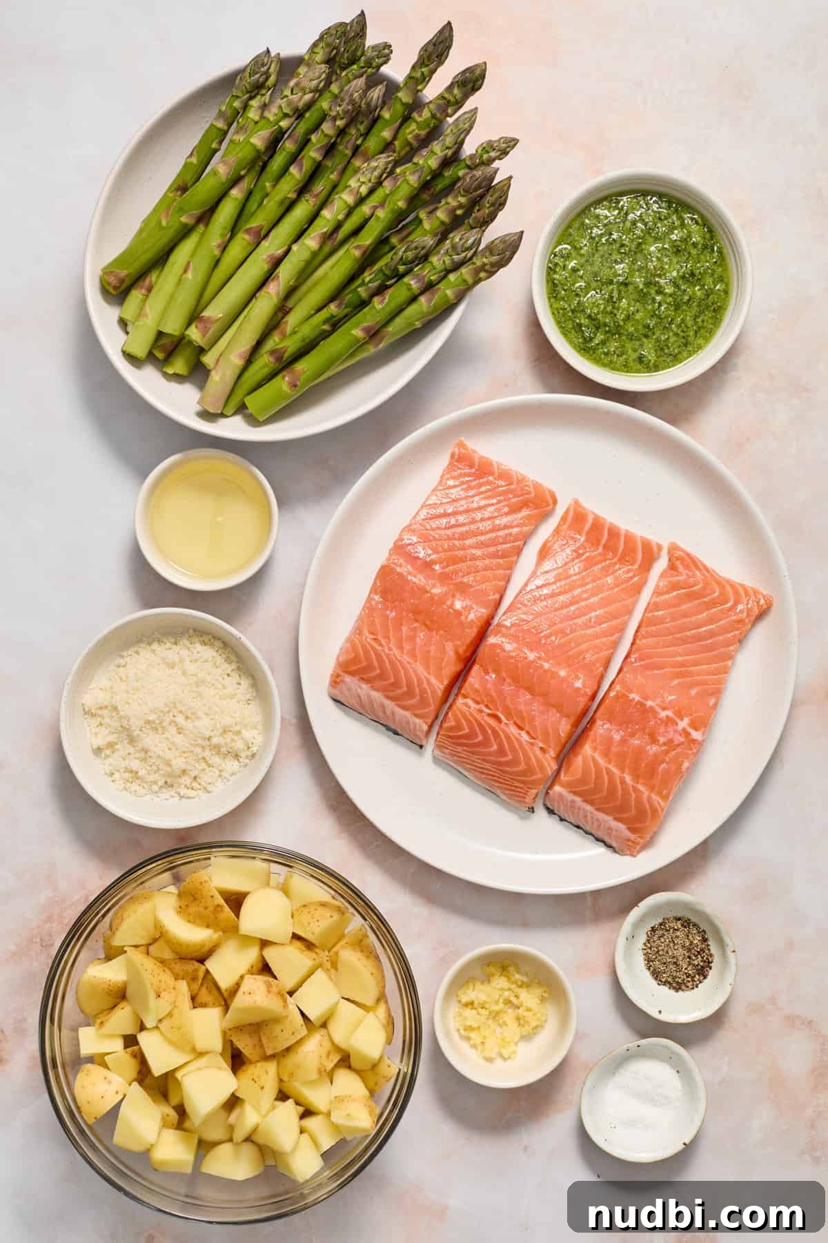 Pesto Salmon Sheet-Pan Dinner with Roasted Veggies 3 Salmon, asparagus, parmesan, potatoes and other ingredients on counter.