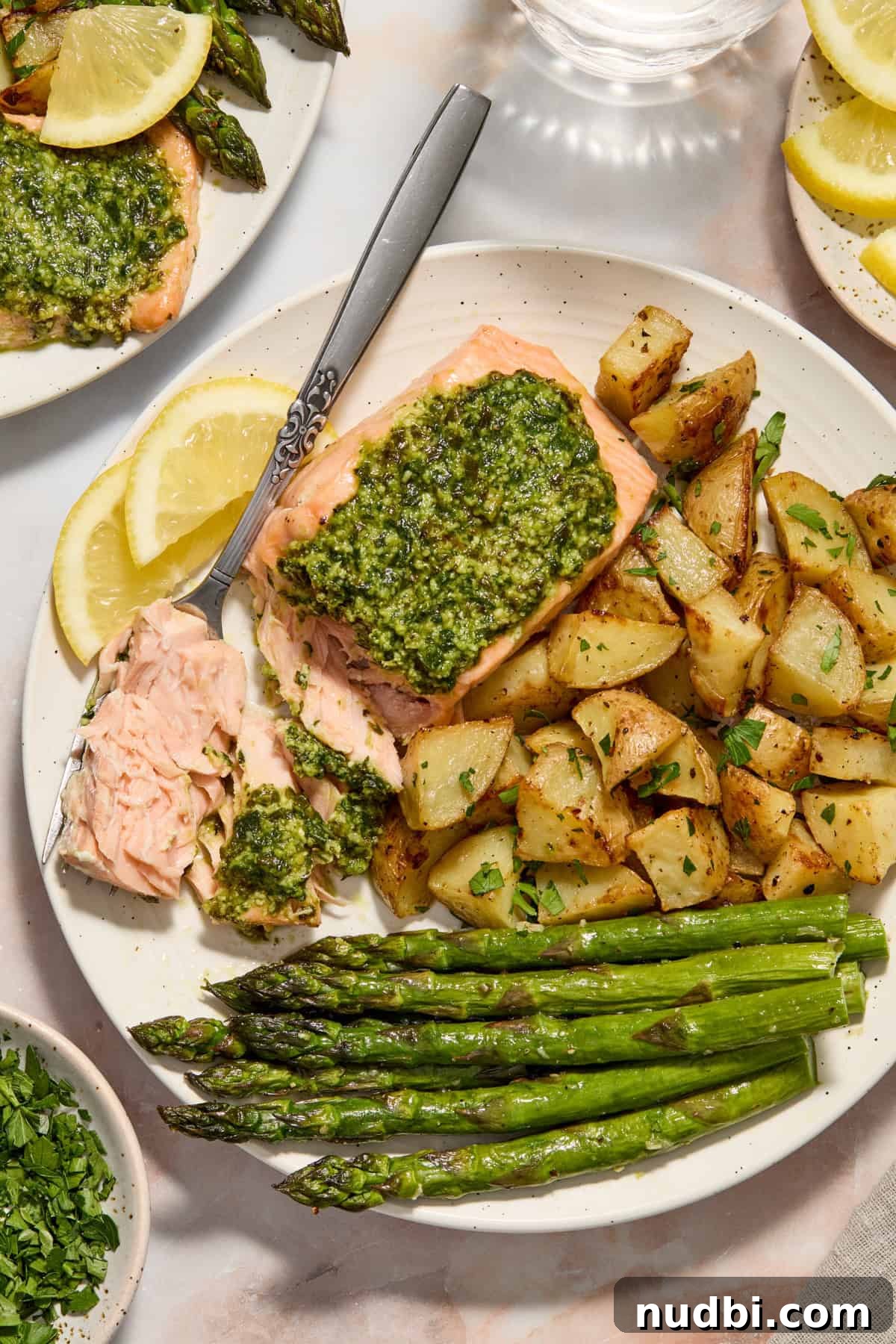 Pesto Salmon Sheet-Pan Dinner with Roasted Veggies 6 Pesto salmon on white plate with fork holding piece of flaked salmon.