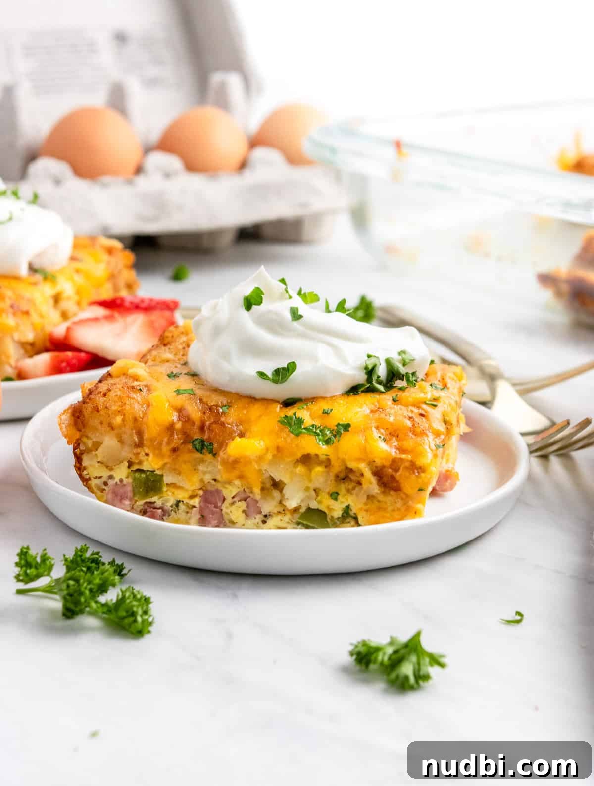 Cheesy Tater Tot Breakfast Casserole with Sausage and Eggs 2 Breakfast casserole with tator tots with sour cream on white plate.