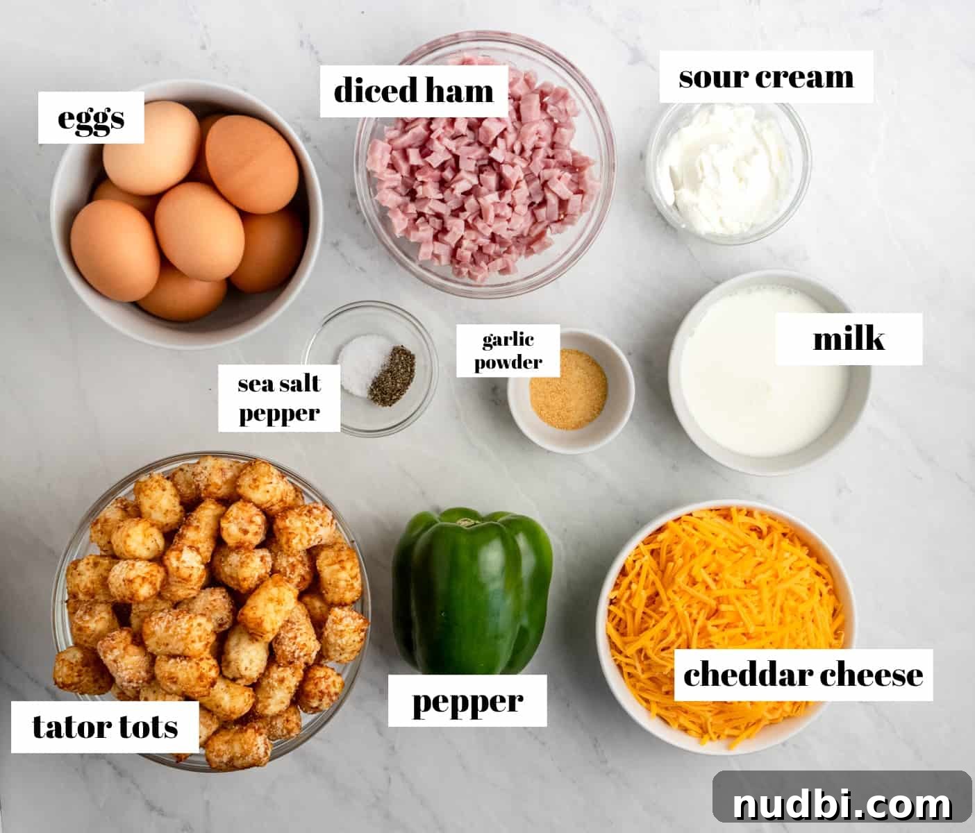 Cheesy Tater Tot Breakfast Casserole with Sausage and Eggs 3 Eggs, ham, pepper, milk and other ingredients labeled on counter.